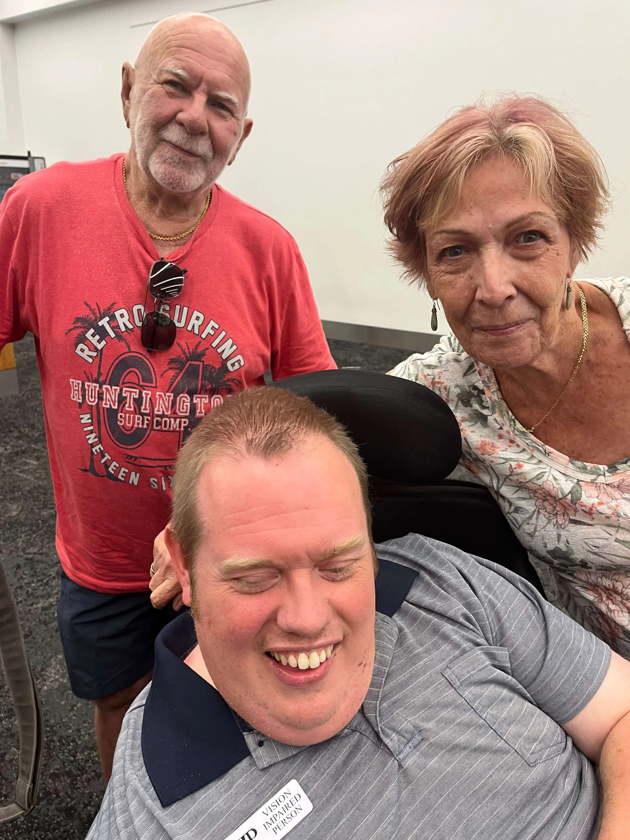 Three older adults and one younger man smiling for a group photo, with the man in a wheelchair in the front and the others standing behind him.