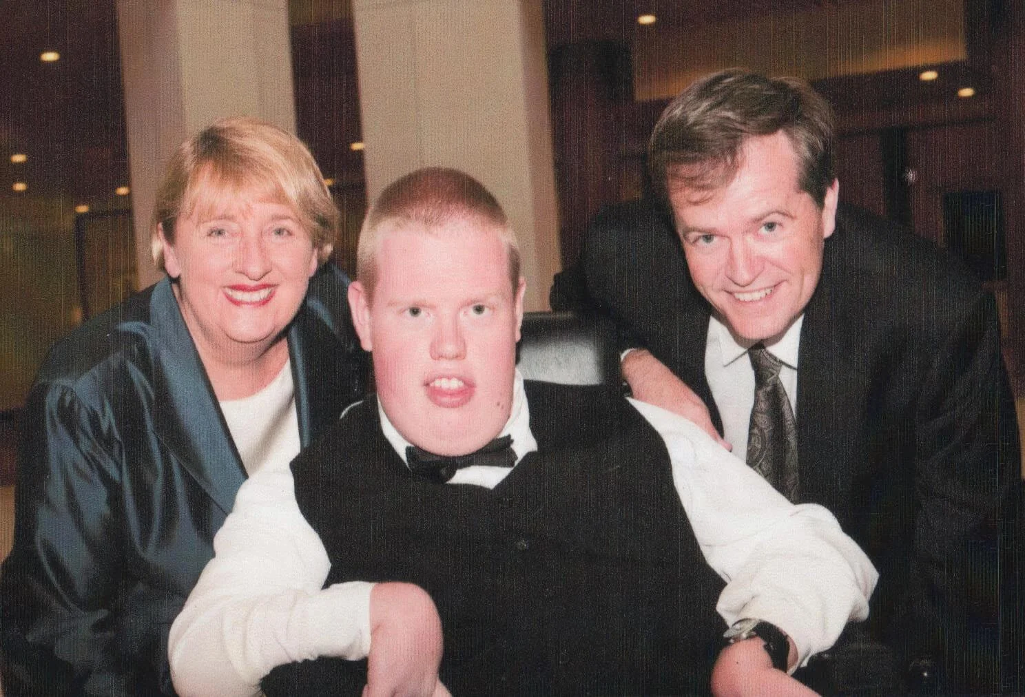 A woman, man, and young man in formal attire posing together indoors.