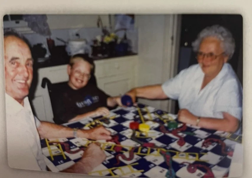 Three people, two adults and one child, playing a board game called Sorry at a kitchen table, smiling and holding game pieces.