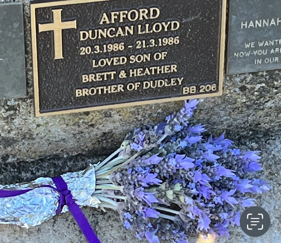 A memorial plaque for Afford Duncan Lloyd, dated March 20-21, 1986, with a purple lavender bouquet laid underneath.