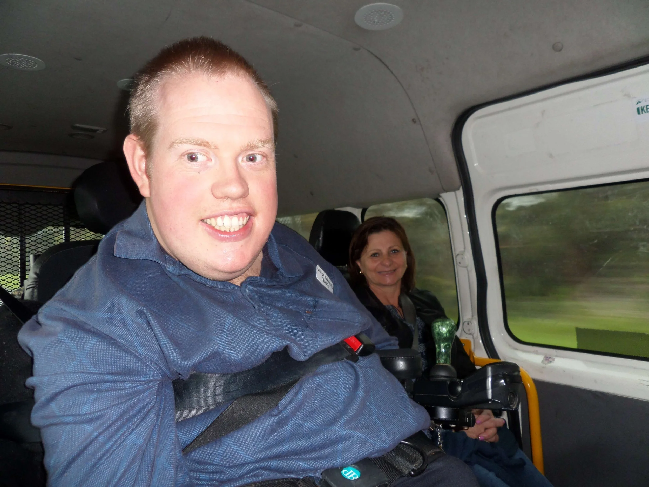 A man and a woman sitting inside a vehicle, with the man in the foreground smiling at the camera.