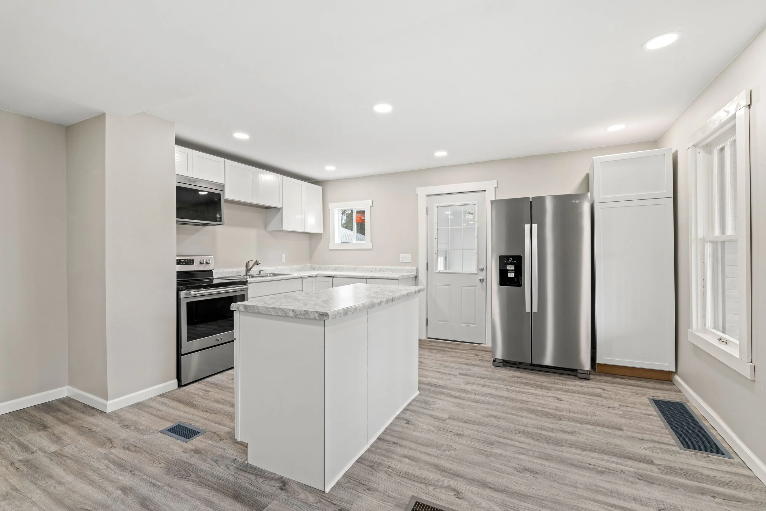Modern kitchen with white cabinets, marble countertops, stainless steel refrigerator, and wood-look flooring.