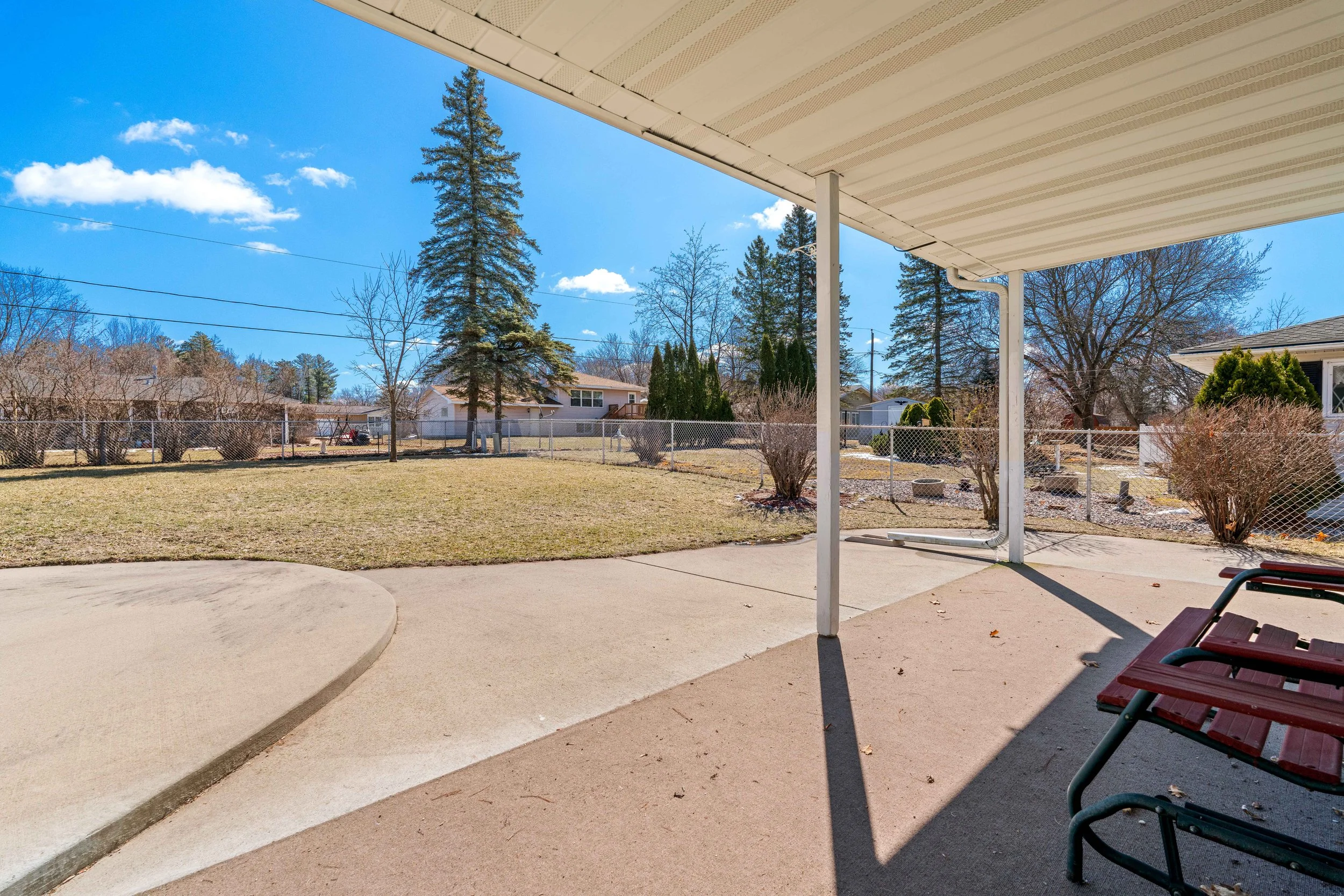 Backyard view with a patio, lawn, trees, and houses in the distance under a clear blue sky