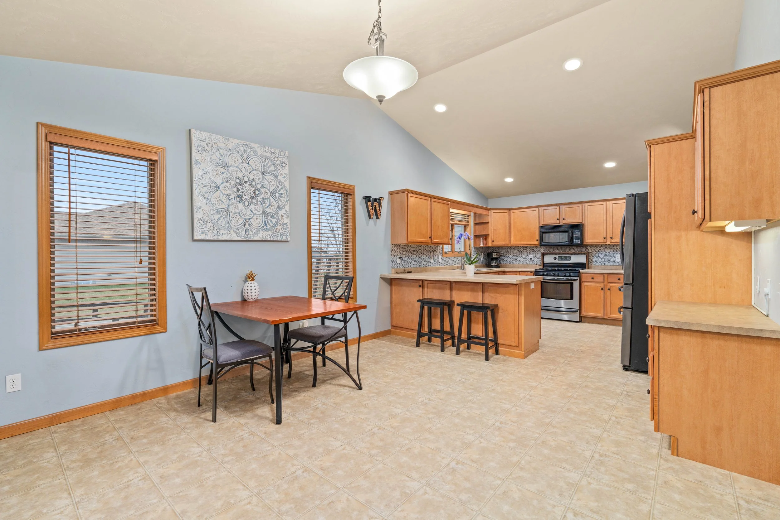 Kitchen with wooden cabinets, black appliances, a small dining table with two chairs, tiled floor, and blue walls.