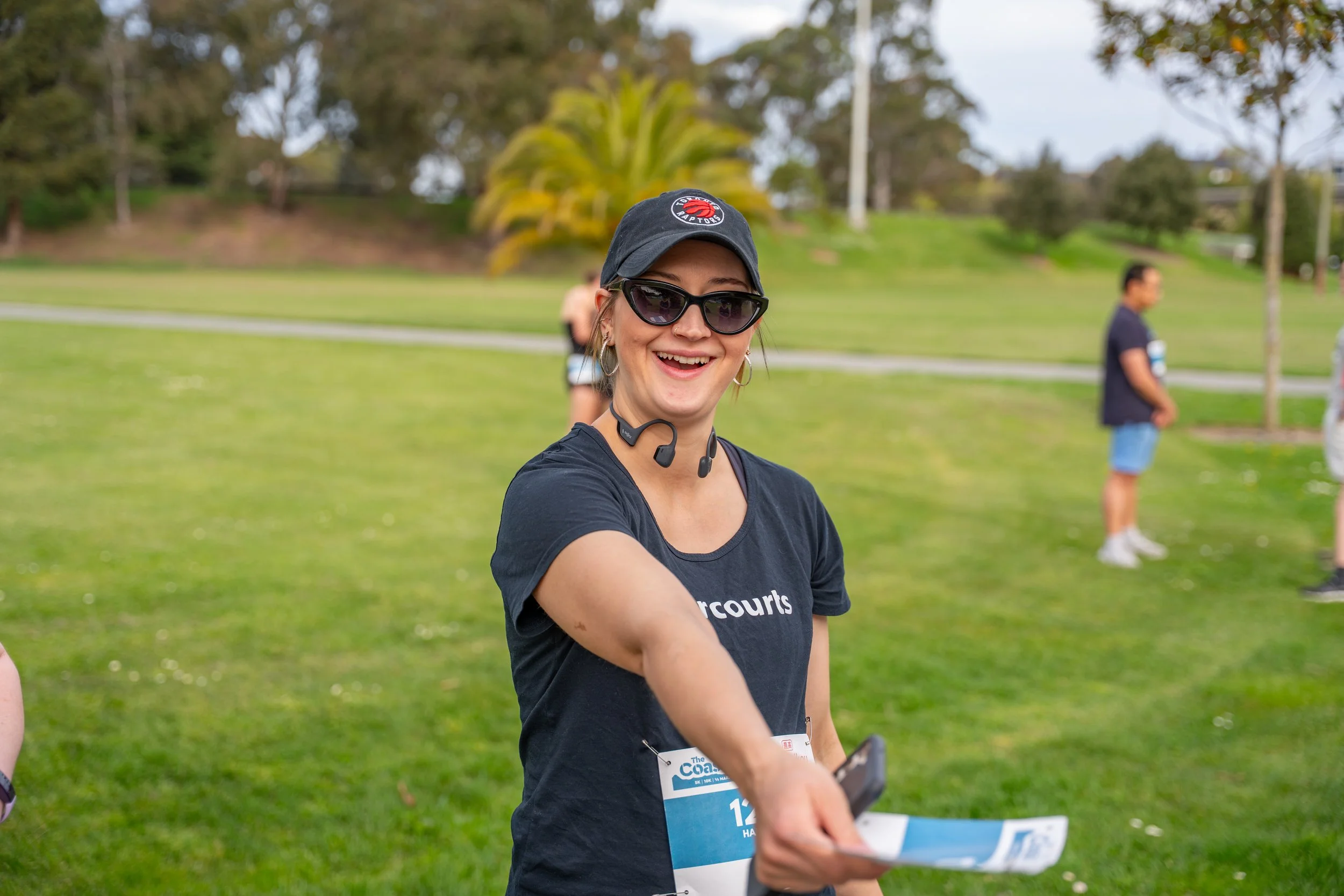 A smiling woman in black sunglasses and a black cap with a Raptors logo, wearing a black t-shirt with 