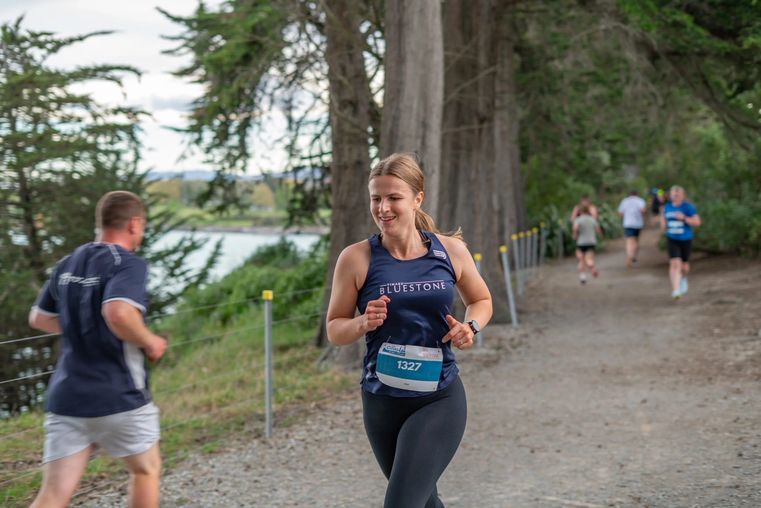 Female runner wearing a blue tank top and black leggings participating in a trail race outdoors.