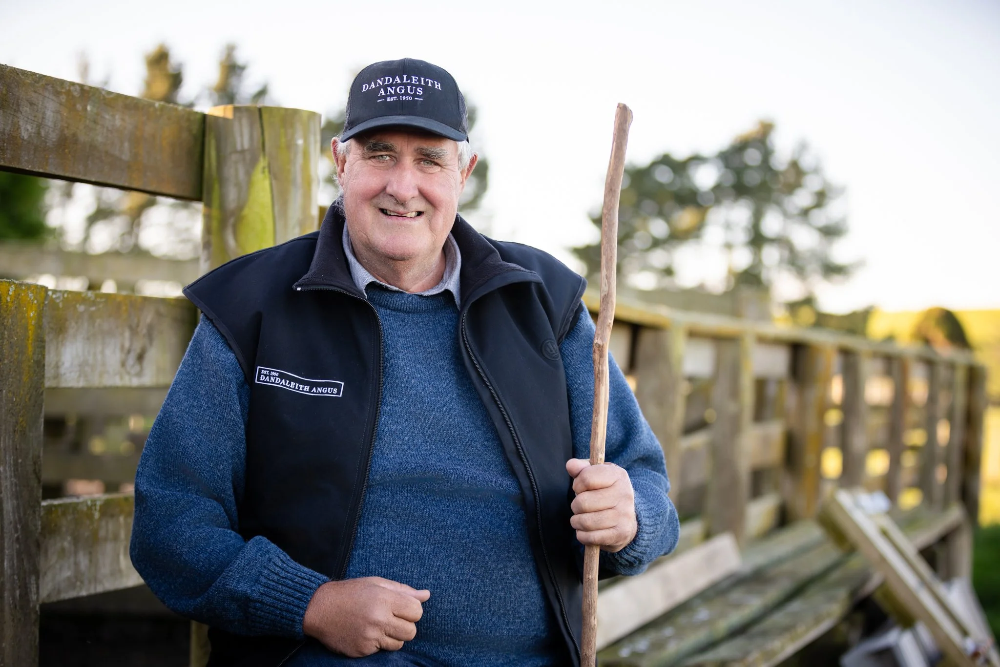 Willy Philip of 'DANDLEITH ANGUS' beside a wooden fence with trees in the background.