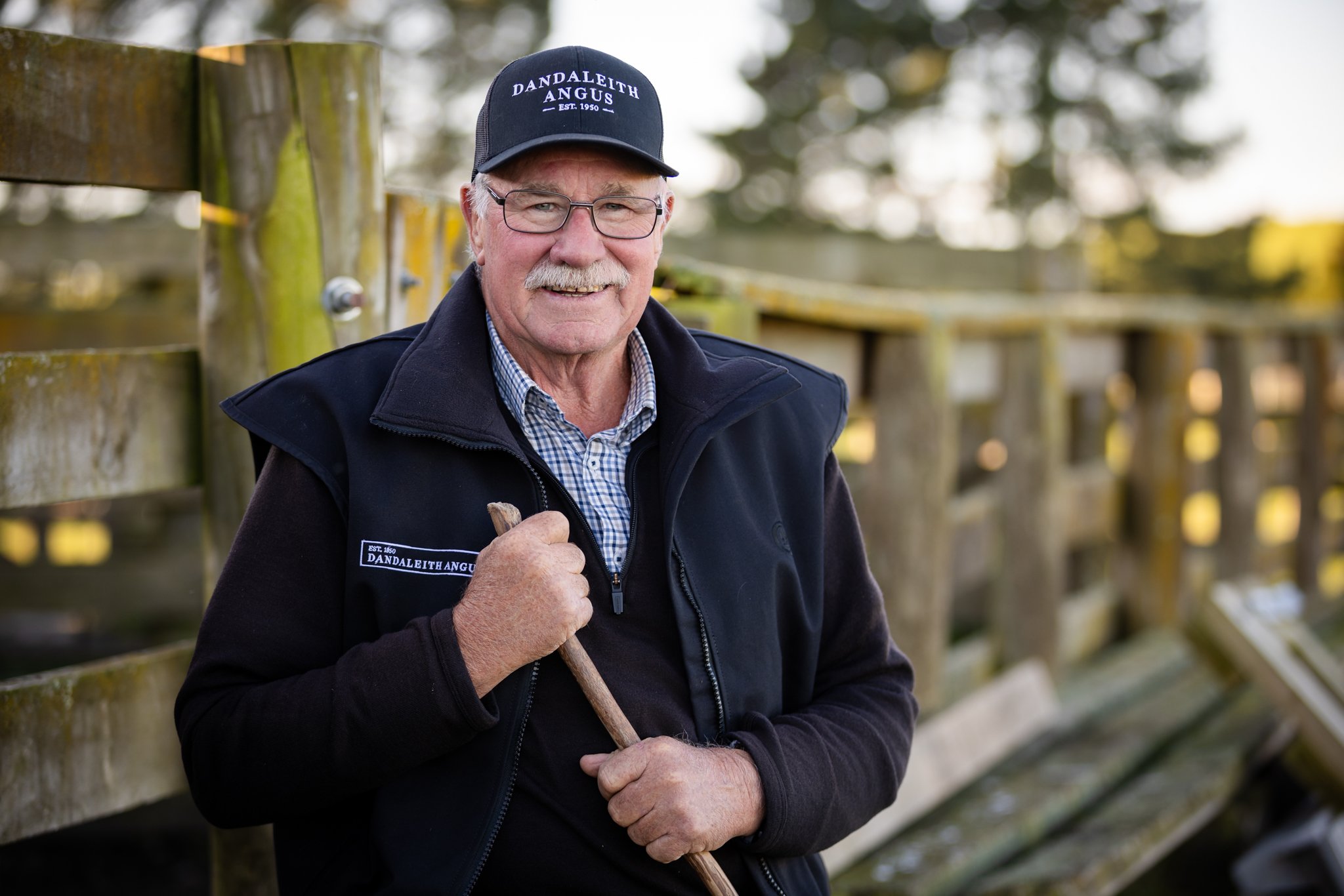 John Philip of 'DANDLEITH ANGUS' beside a wooden fence with trees in the background.