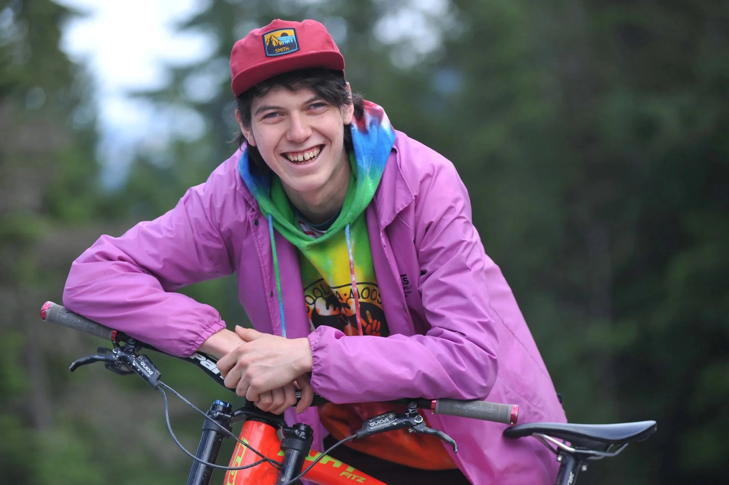 Youth wearing purple jacket sitting on a bike and smiling outdoors.