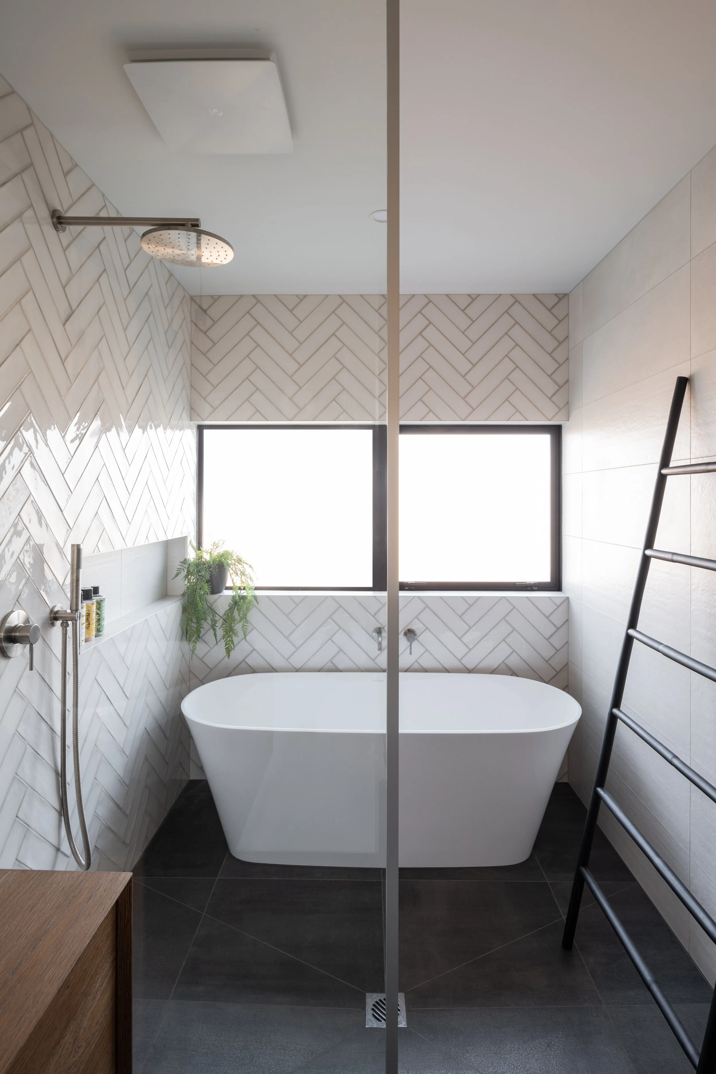 Modern bathroom with a standalone bathtub, large window, black towel rack, and a plant on the window ledge.