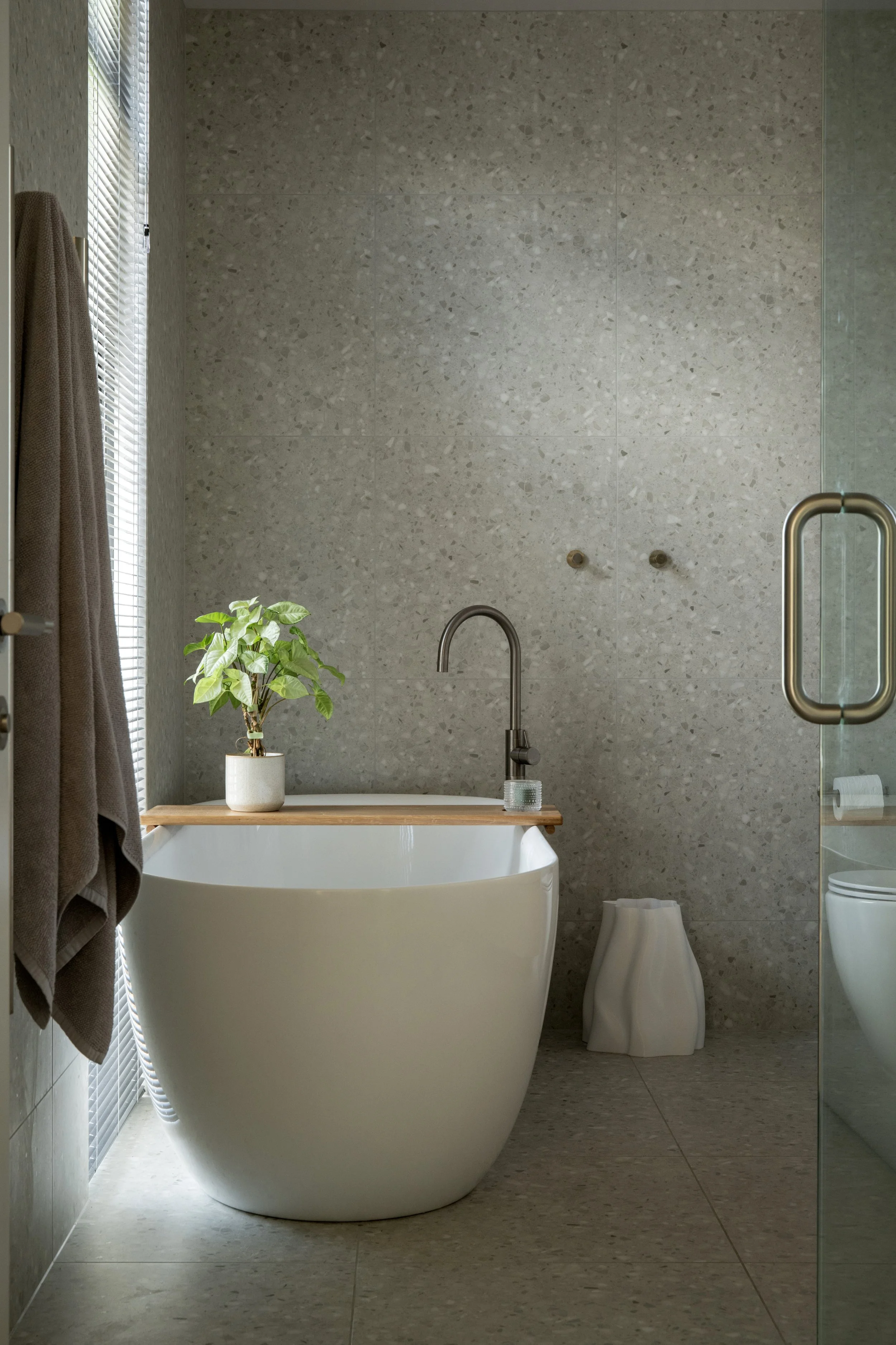 Modern bathroom with a freestanding bathtub, potted plant, and textured gray walls.