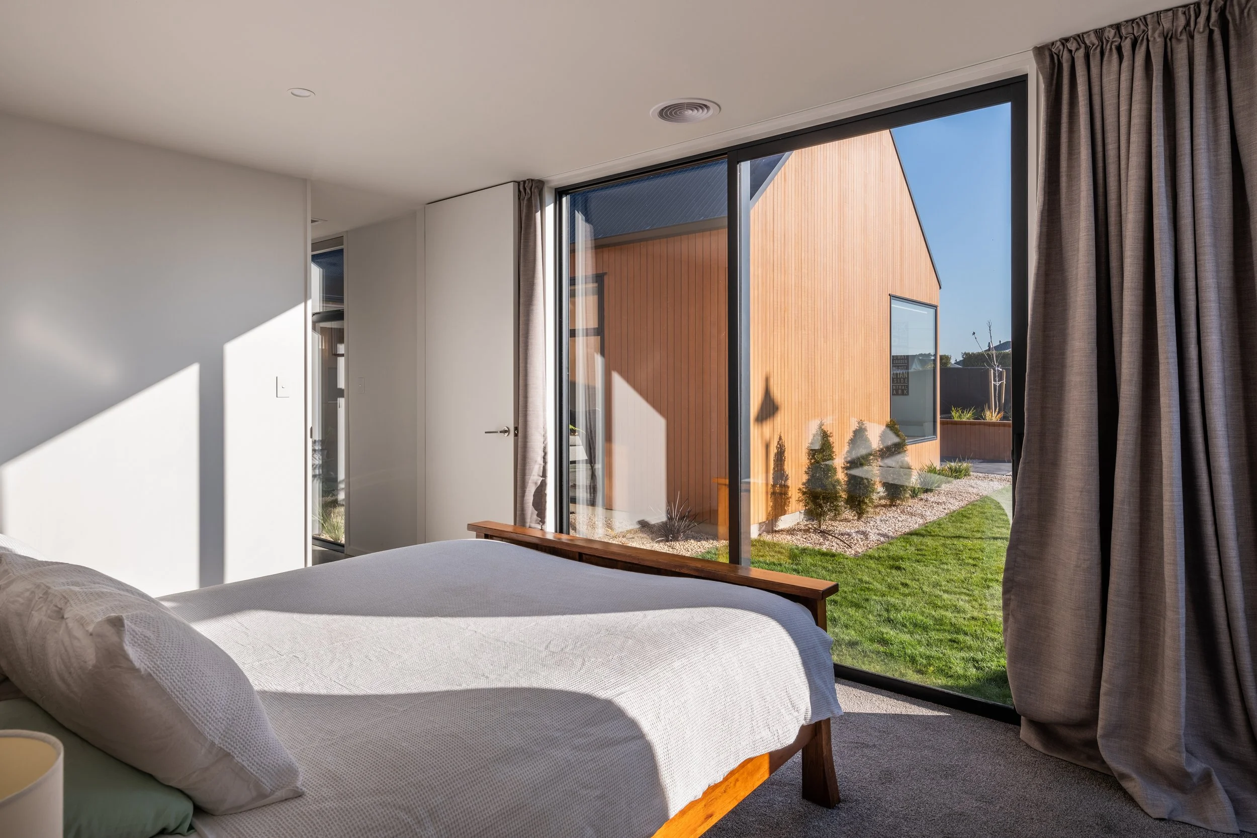 A bedroom with a large sliding glass door showing a yard with grass, small trees, and a wooden building outside.