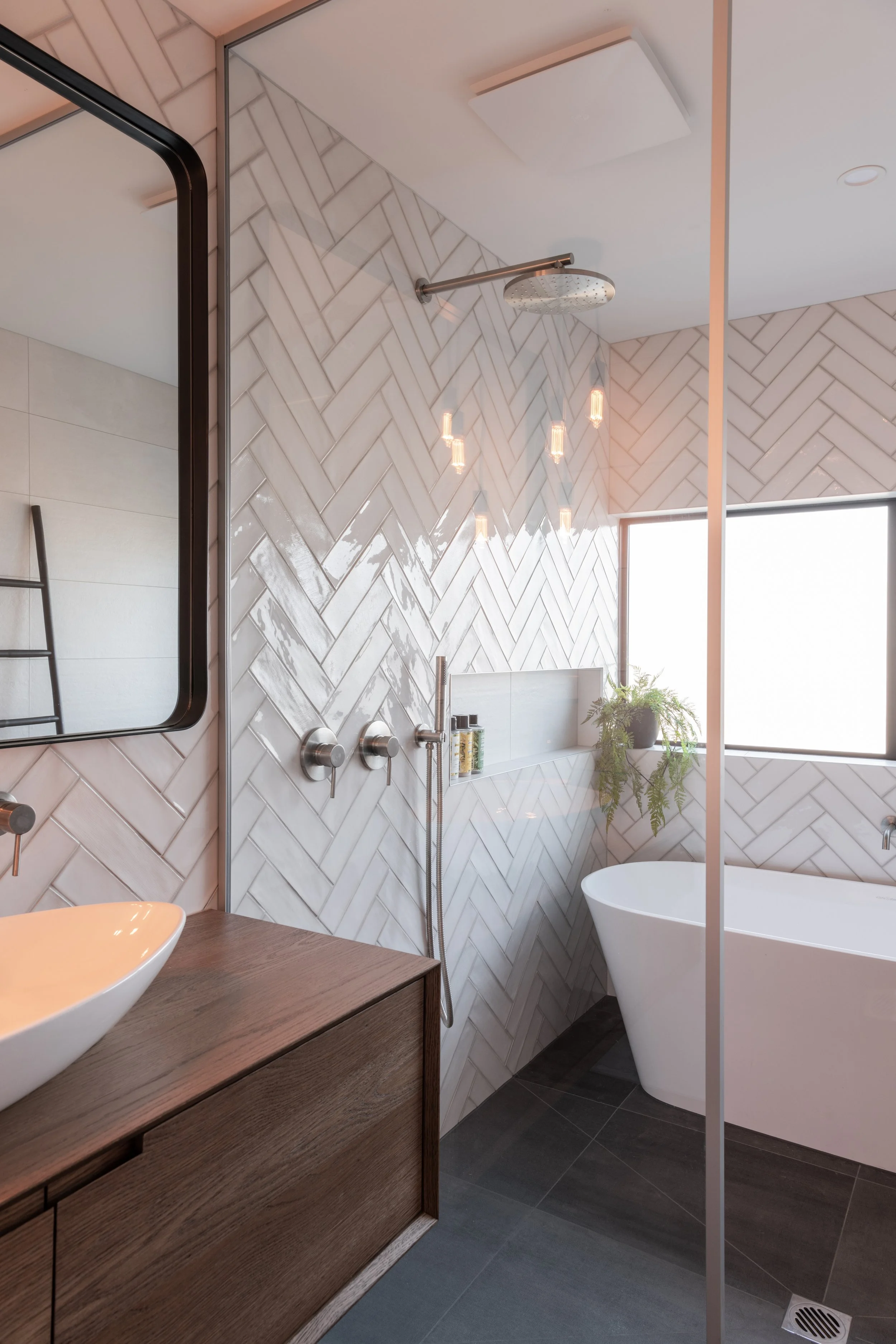Modern bathroom with a walk-in shower, a freestanding bathtub, a wooden vanity with a vessel sink, a large mirror, and a window with a potted plant.