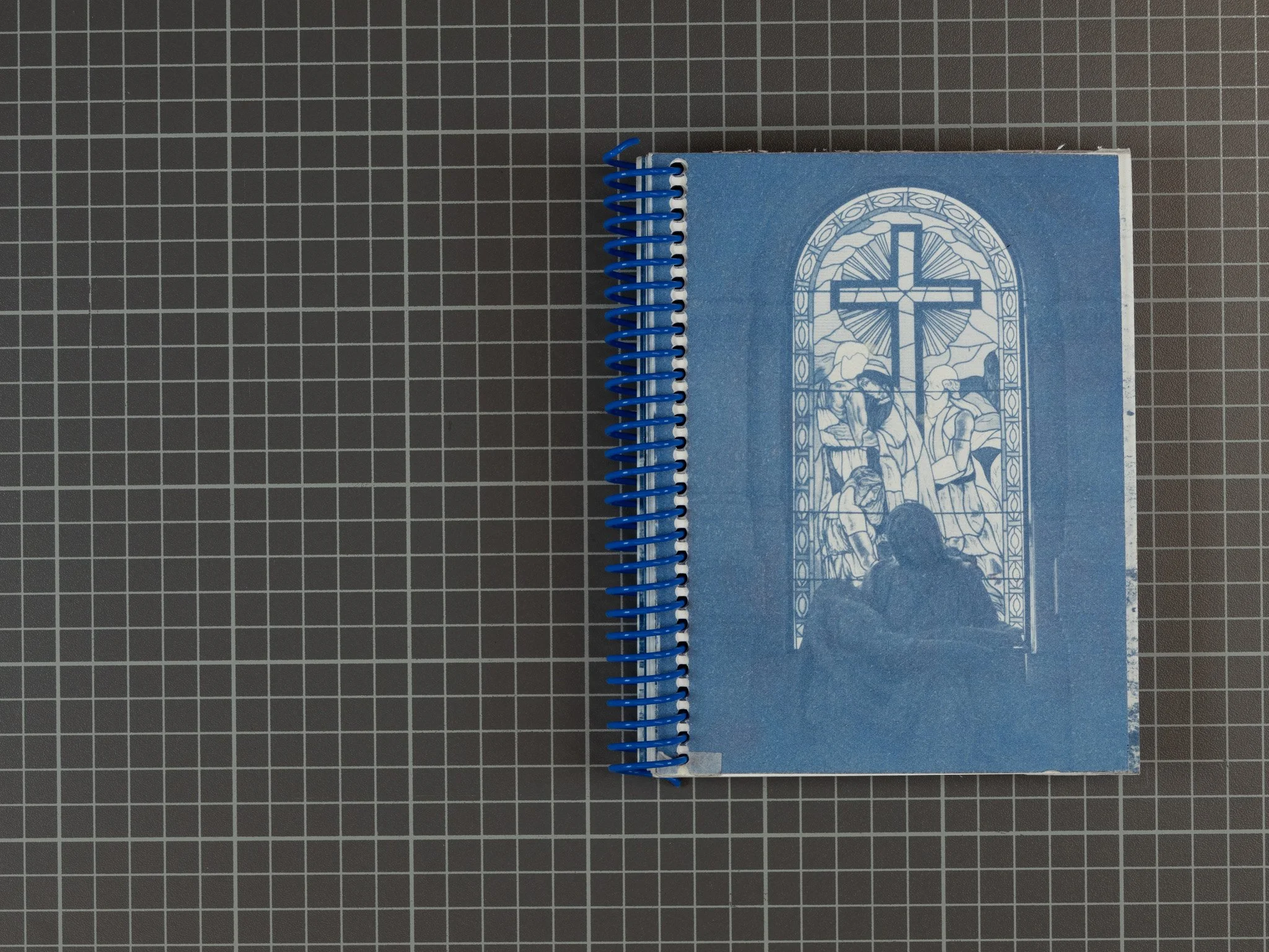 Spiral-bound cyanotype book with a blue cover featuring a stained glass window design, and copy of Michelangelo's Pieta