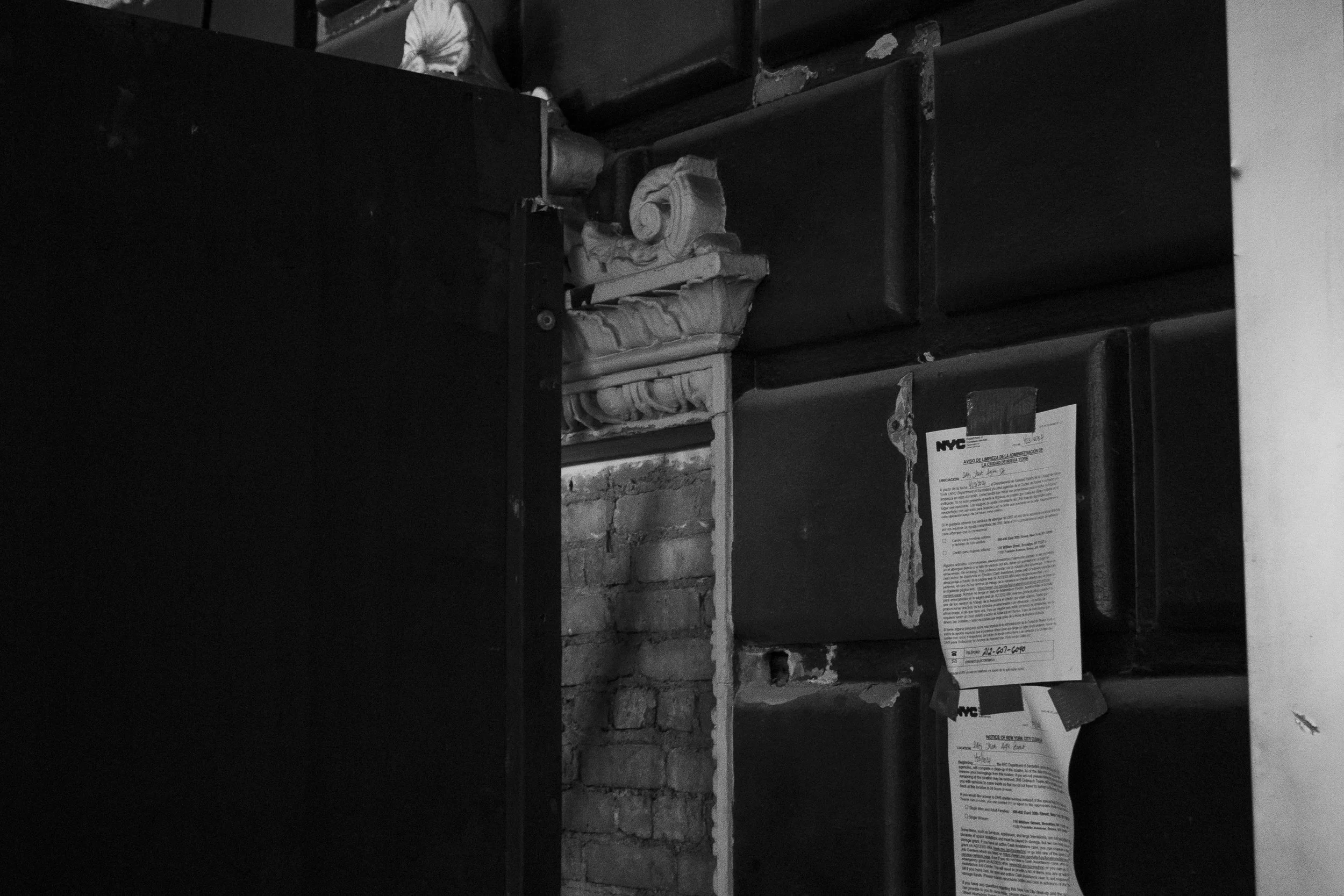 Black and white photo of stacks of boxes and papers in a storage room with brick wall in background.