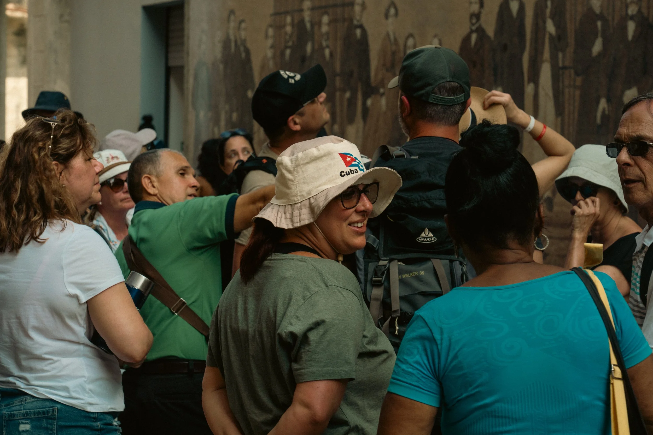 Group of tourists and guides gathered inside a museum near a large wall painting.