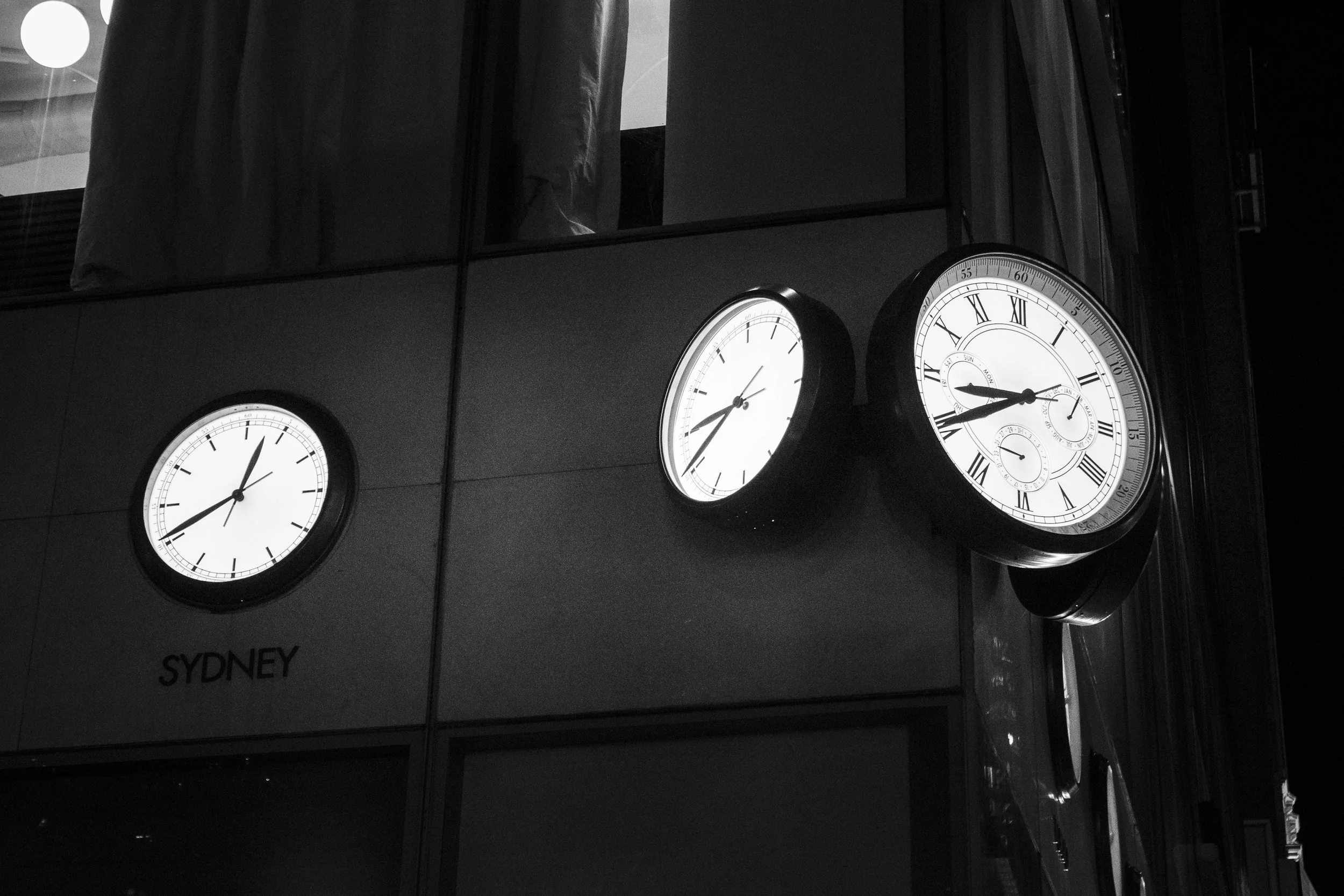 Three clocks mounted on a wall, one showing 1:38, another 2:18, and the third 10:13, with the word 'SYDNEY' below the left clock.