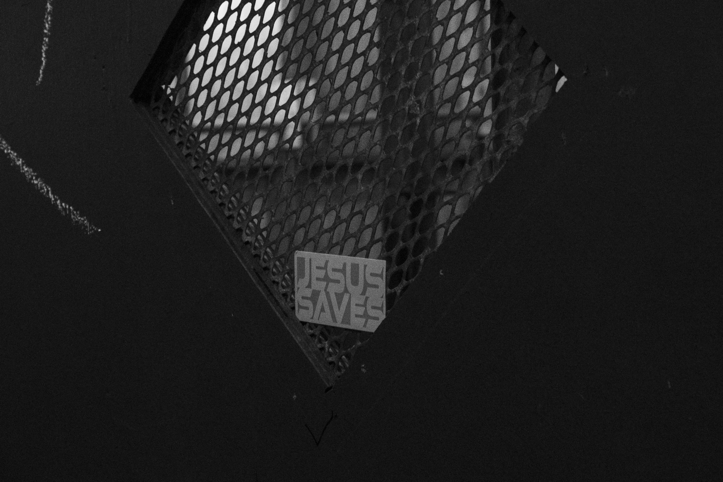 A black and white image of a wall vent with a sticker that reads 'JESUS SAVES' in capital letters.