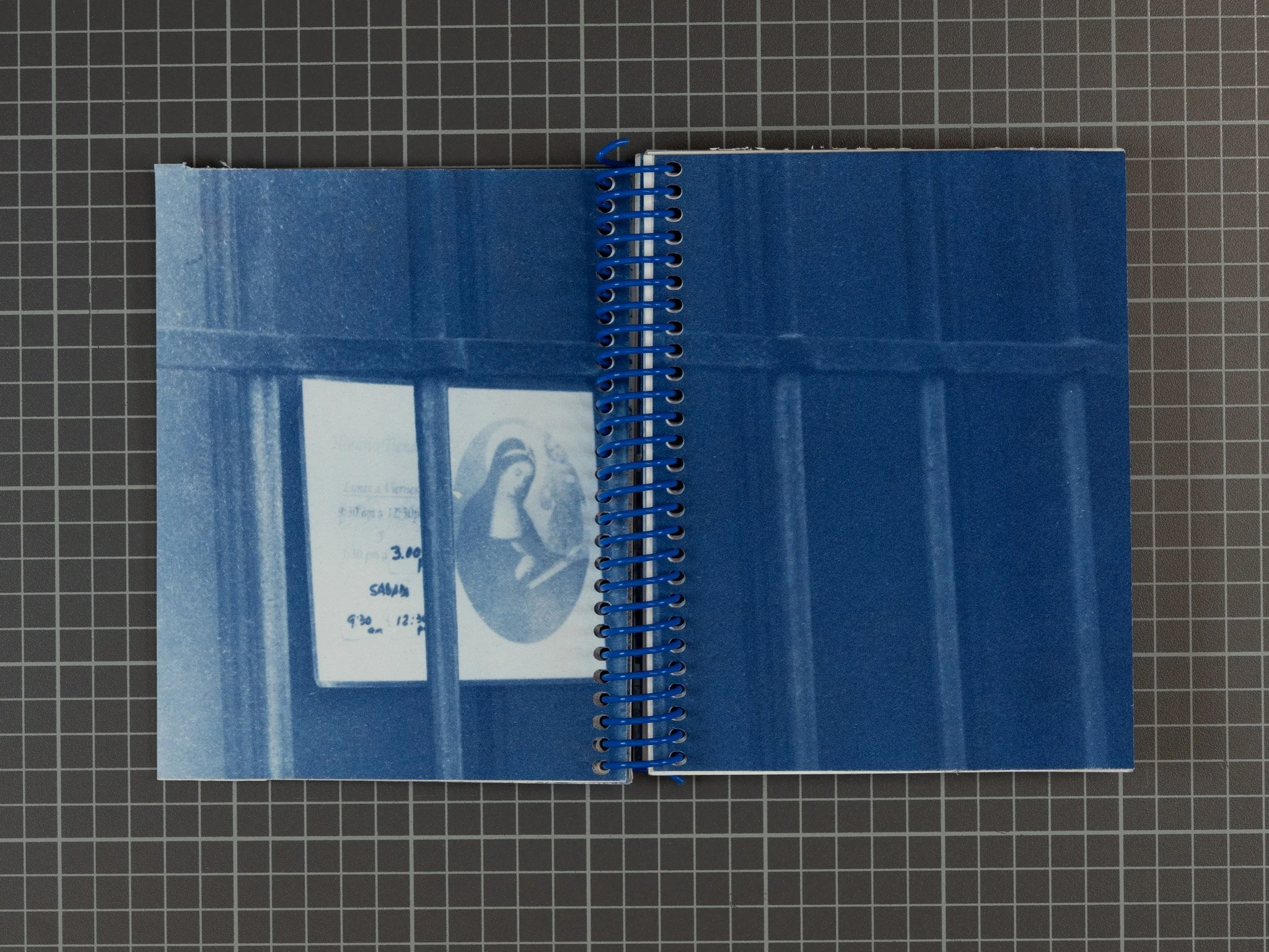 An open spiral cyanotype book with image of school sign featuring madonna reading behind iron bars.