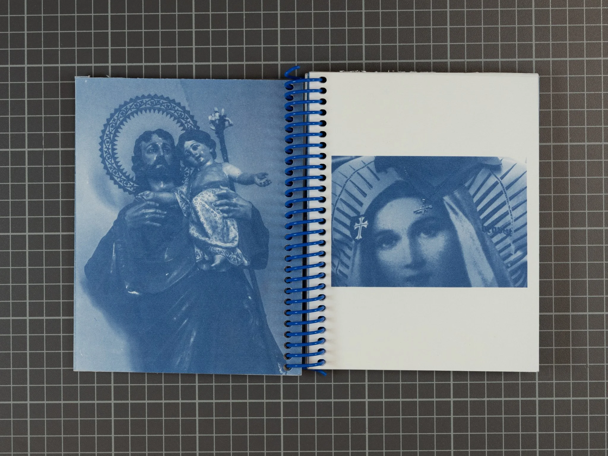 Open sketchbook with two pages; left page features a blue monochrome print of a religious statue of Jesus holding a child, with a halo behind their heads, and a cross above them. right page has a smaller, distorted image of a woman's face with a halo