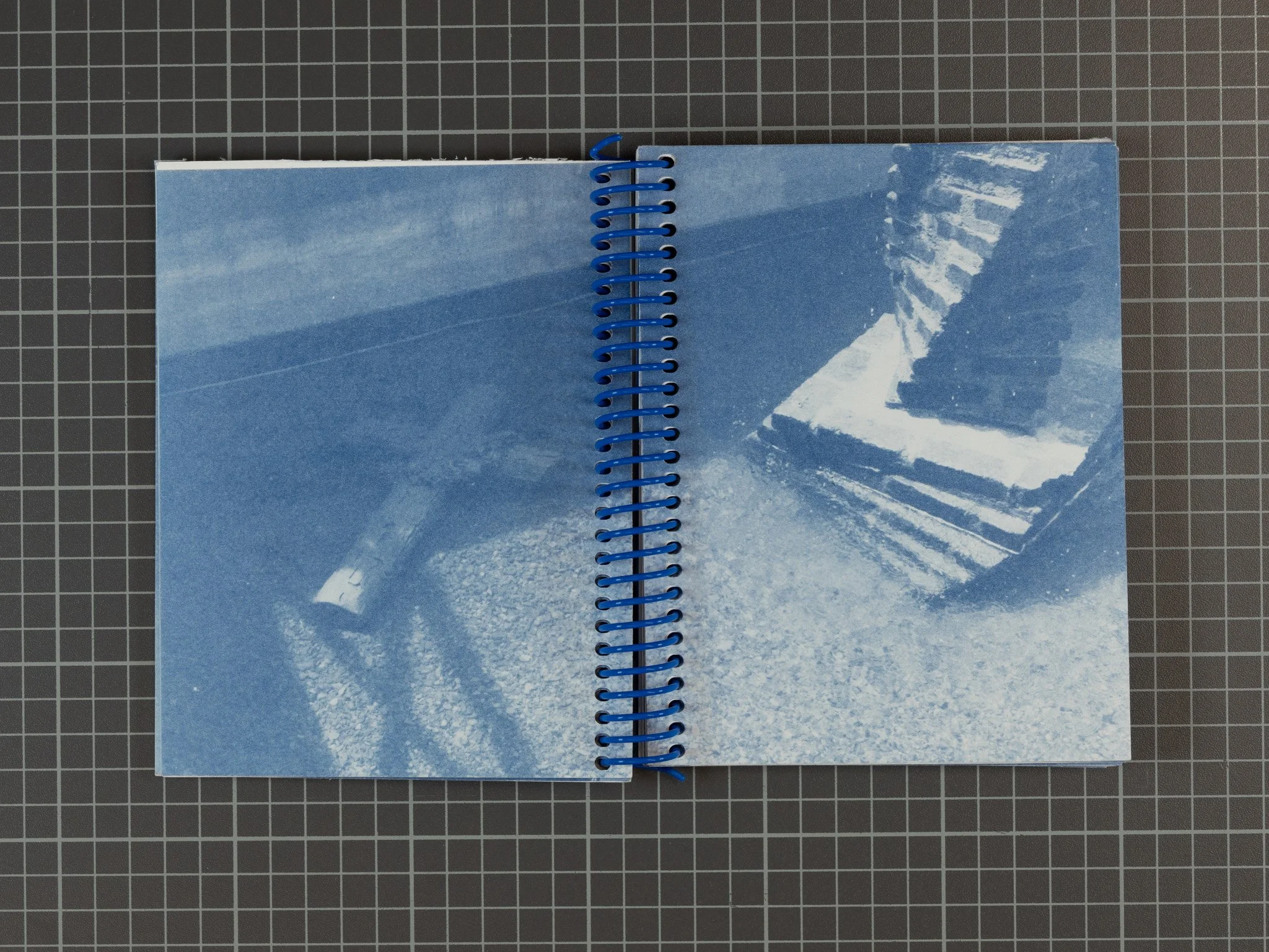 Open spiral-bound notebook with blue-toned photographic pages of stairs and a handrail, placed on a black grid-patterned surface.