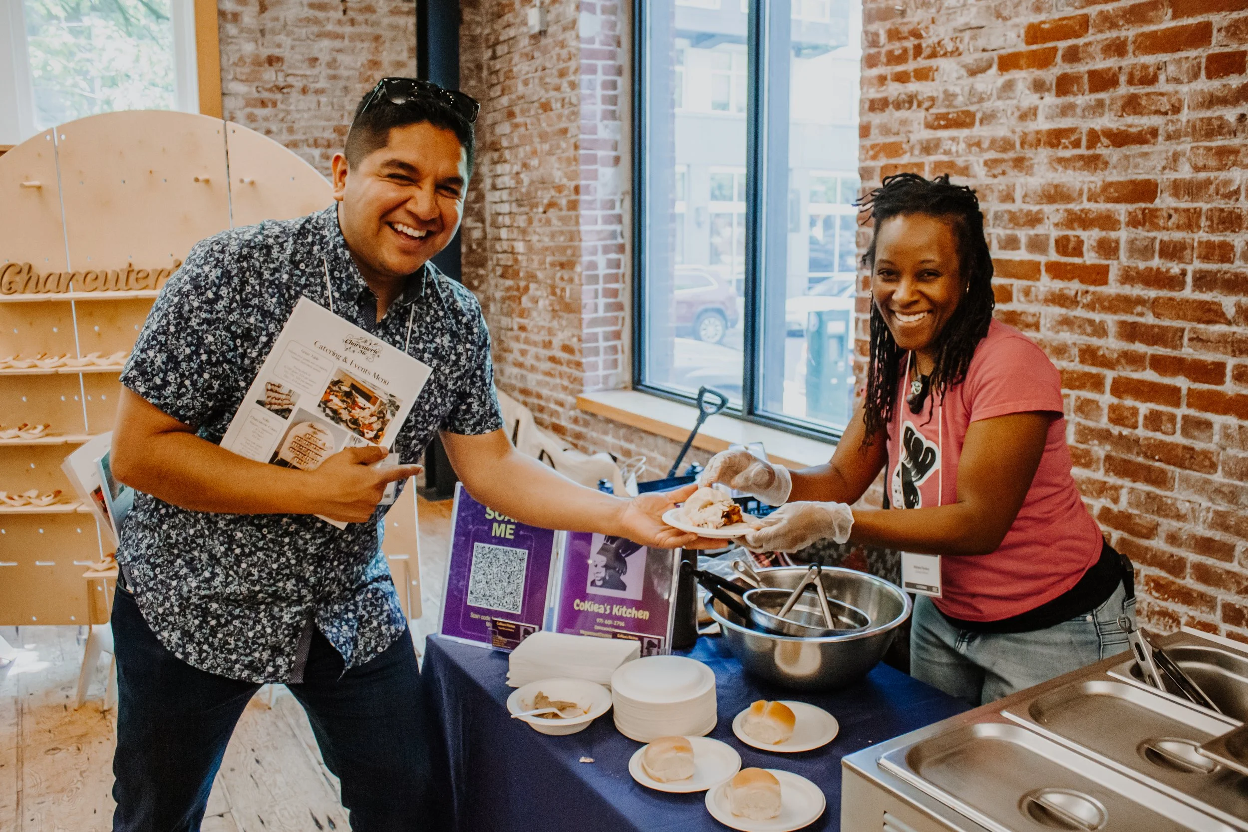 A man receives a plate of food from a woman at the Mercatus Catering Event in Portland