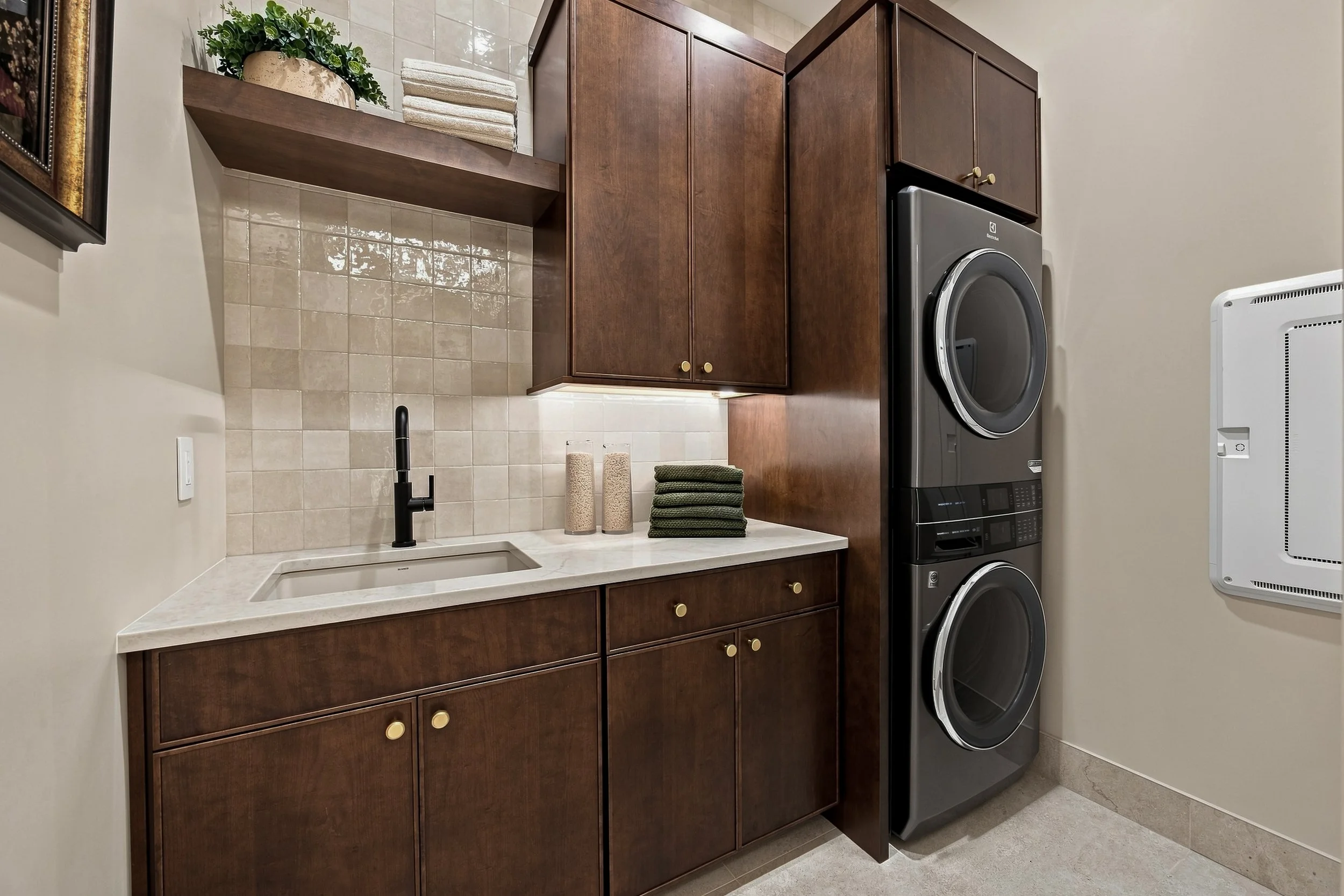 Laundry room with wood cabinetry, pale counters, and stacked appliances.
