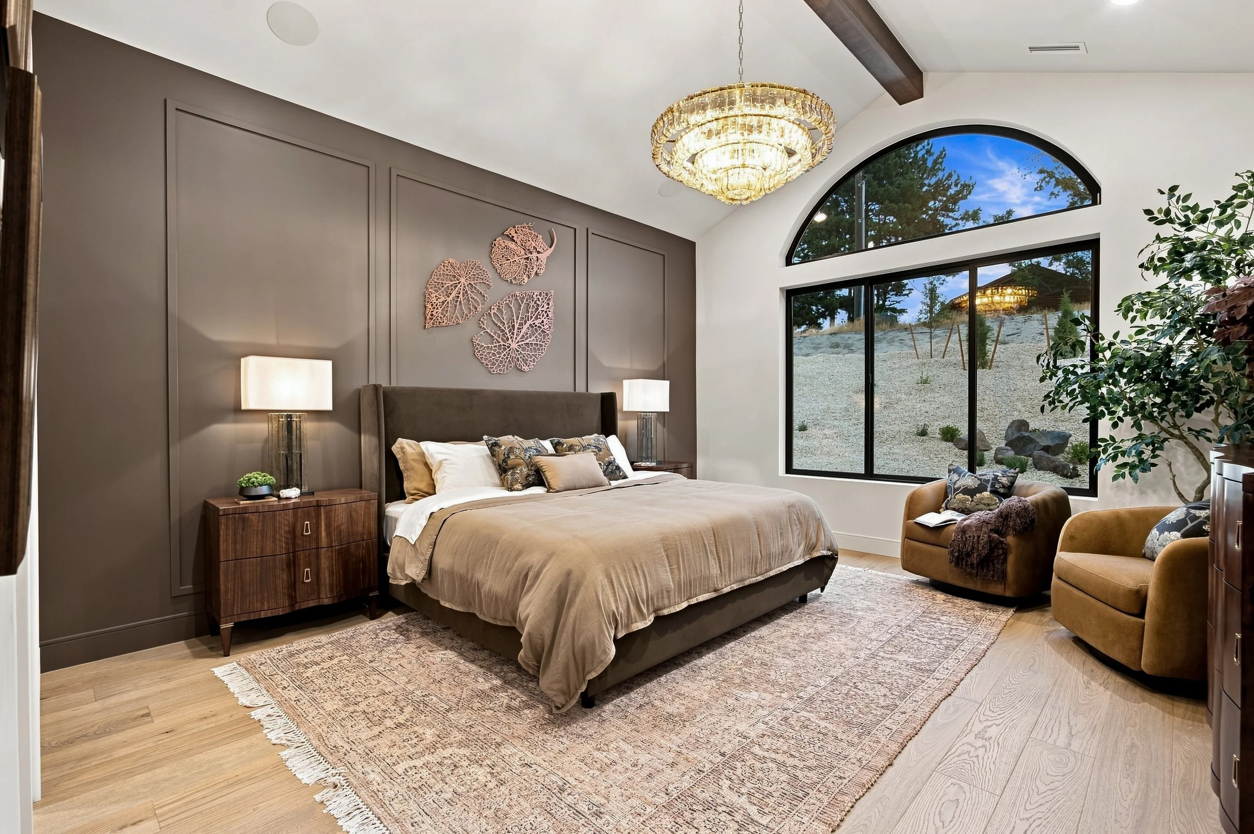 Primary bedroom with a statement chandelier, ceiling fan, and arched window.