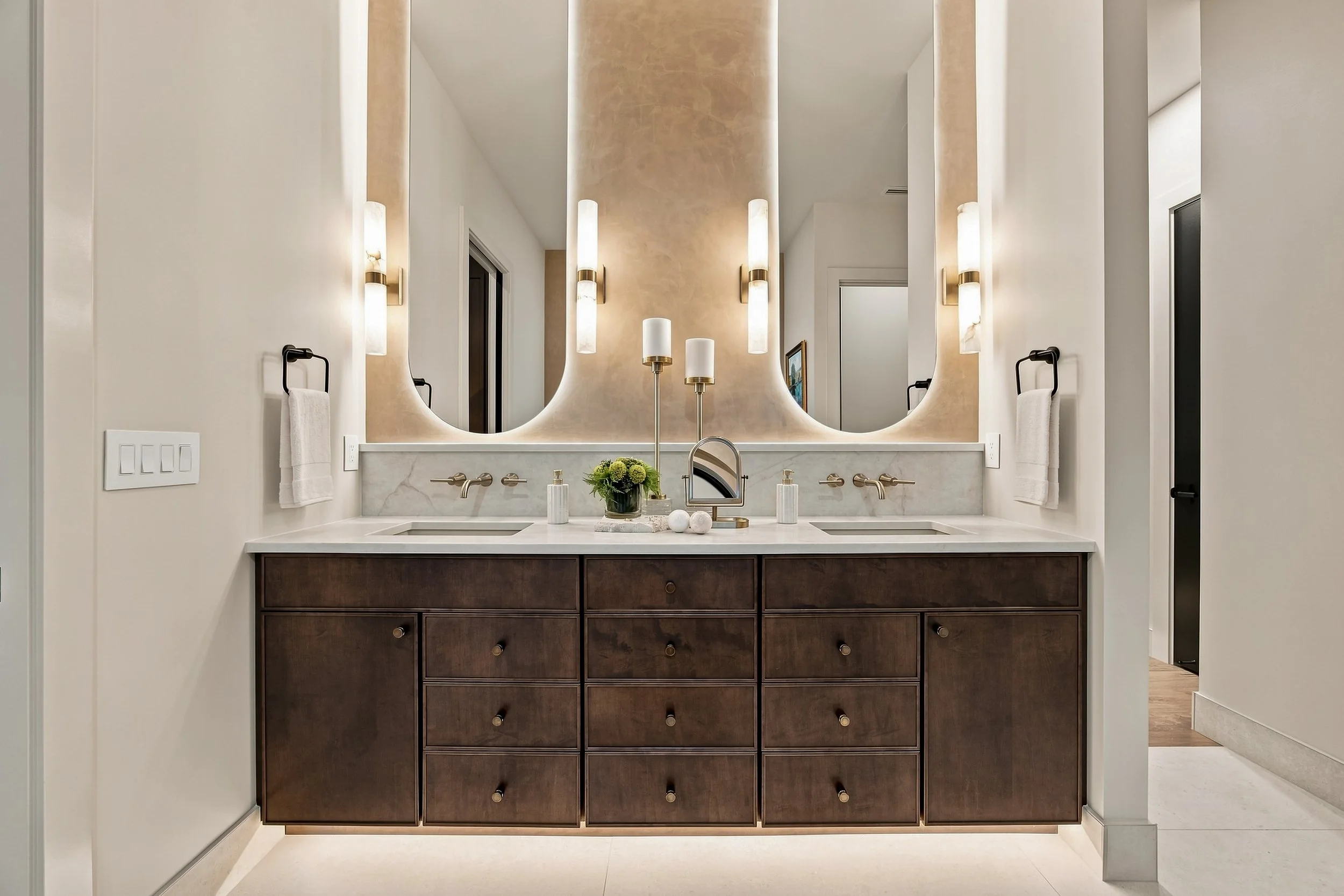 Primary bathroom with paired mirrors, wall sconces, and wood vanity cabinetry.