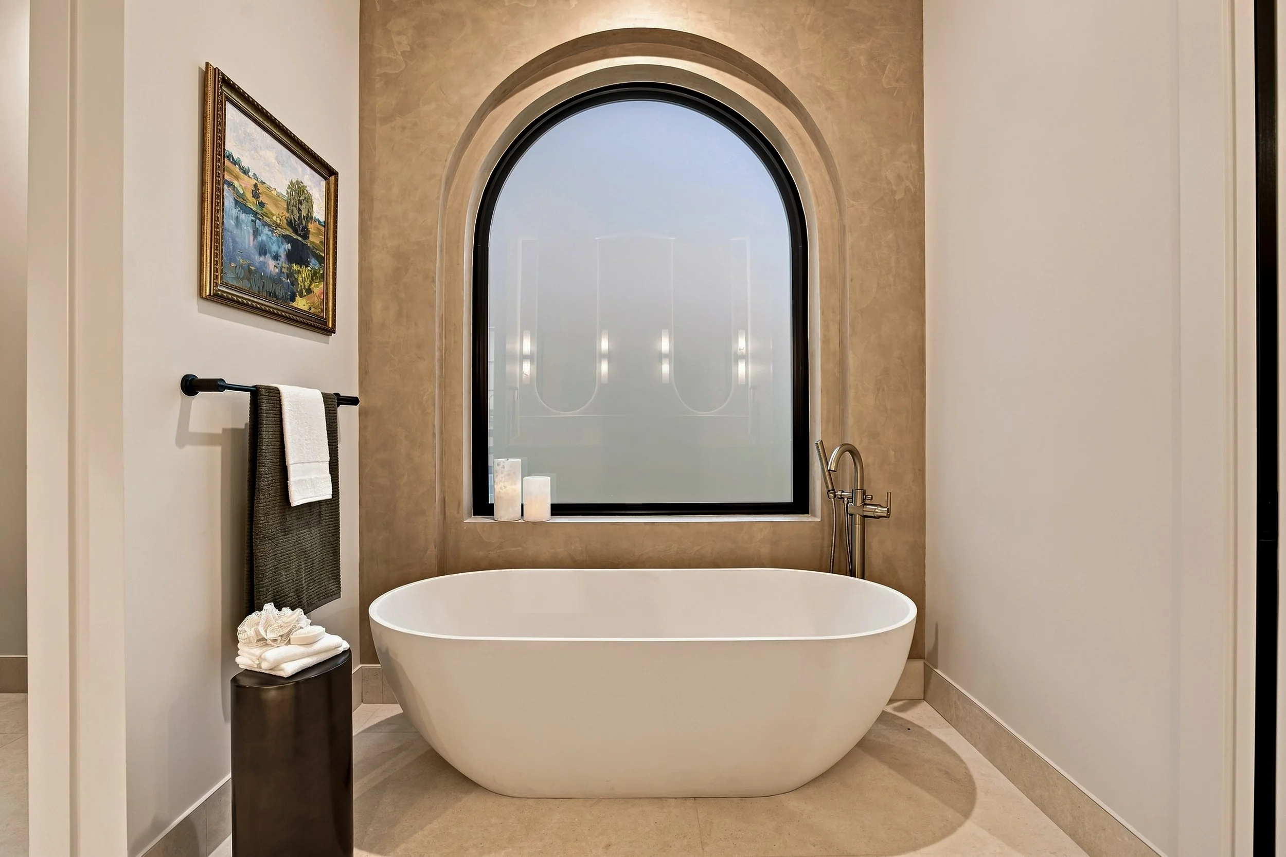 Freestanding bathtub beneath a stepped arched window with concealed lighting.
