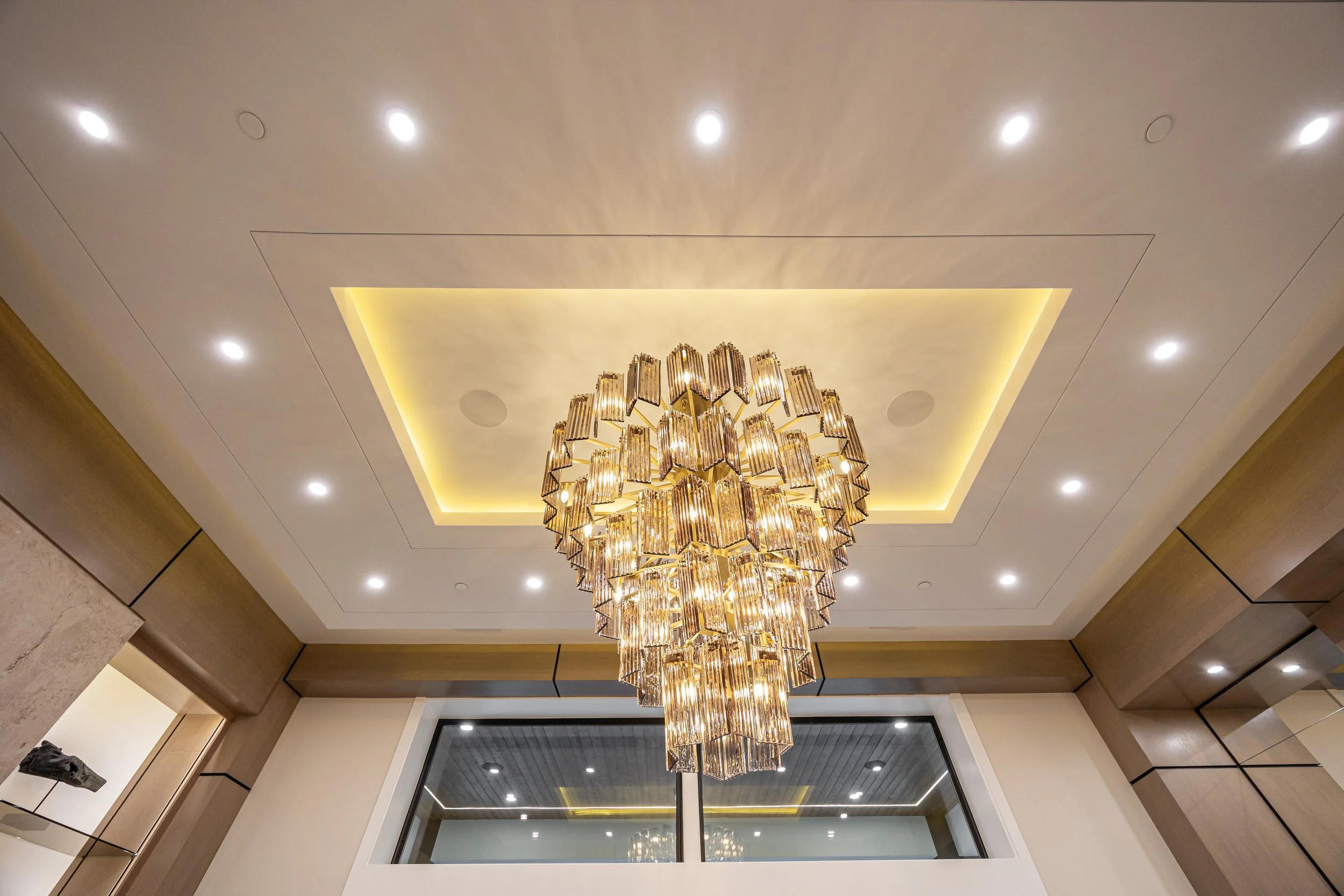 Sculptural chandelier, recessed downlights, and illuminated ceiling detailing in the Overture living room.
