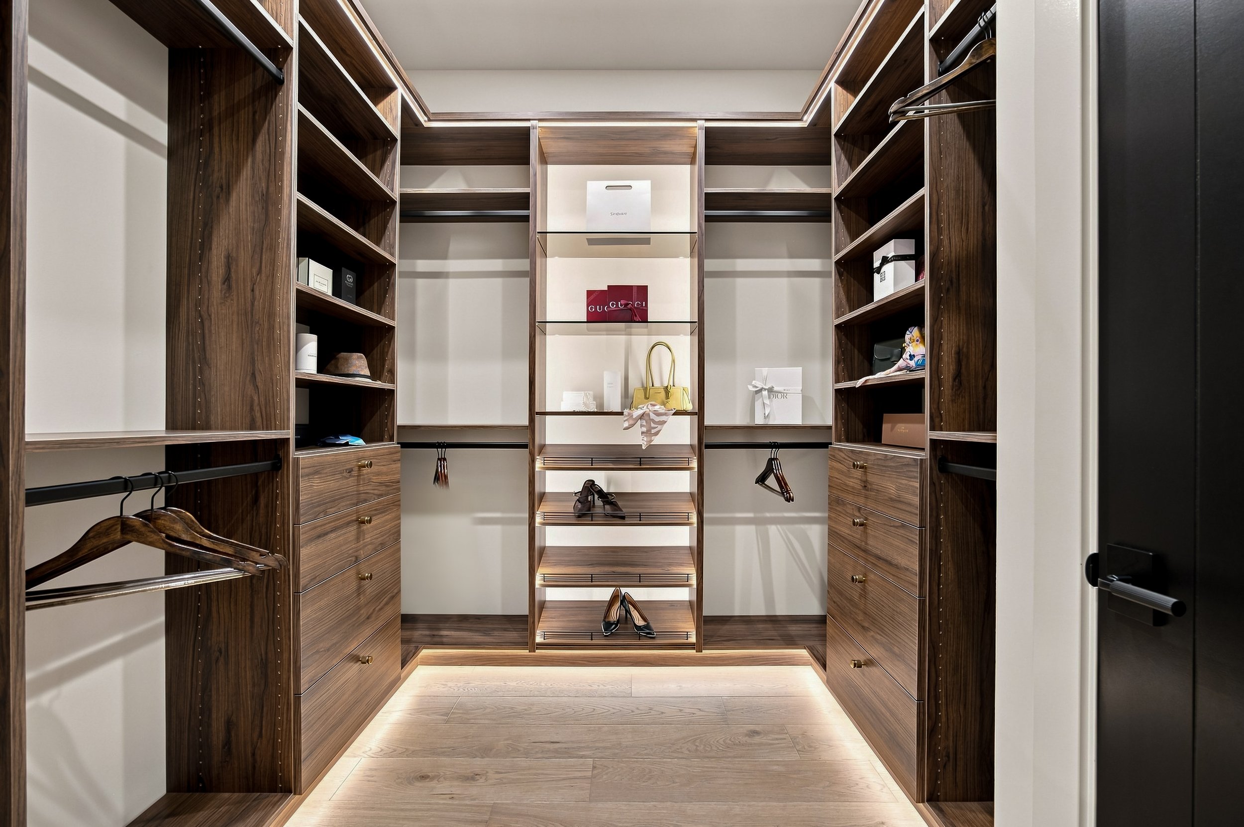Walk-in primary closet with wood cabinetry, open shelving, and integrated lighting.