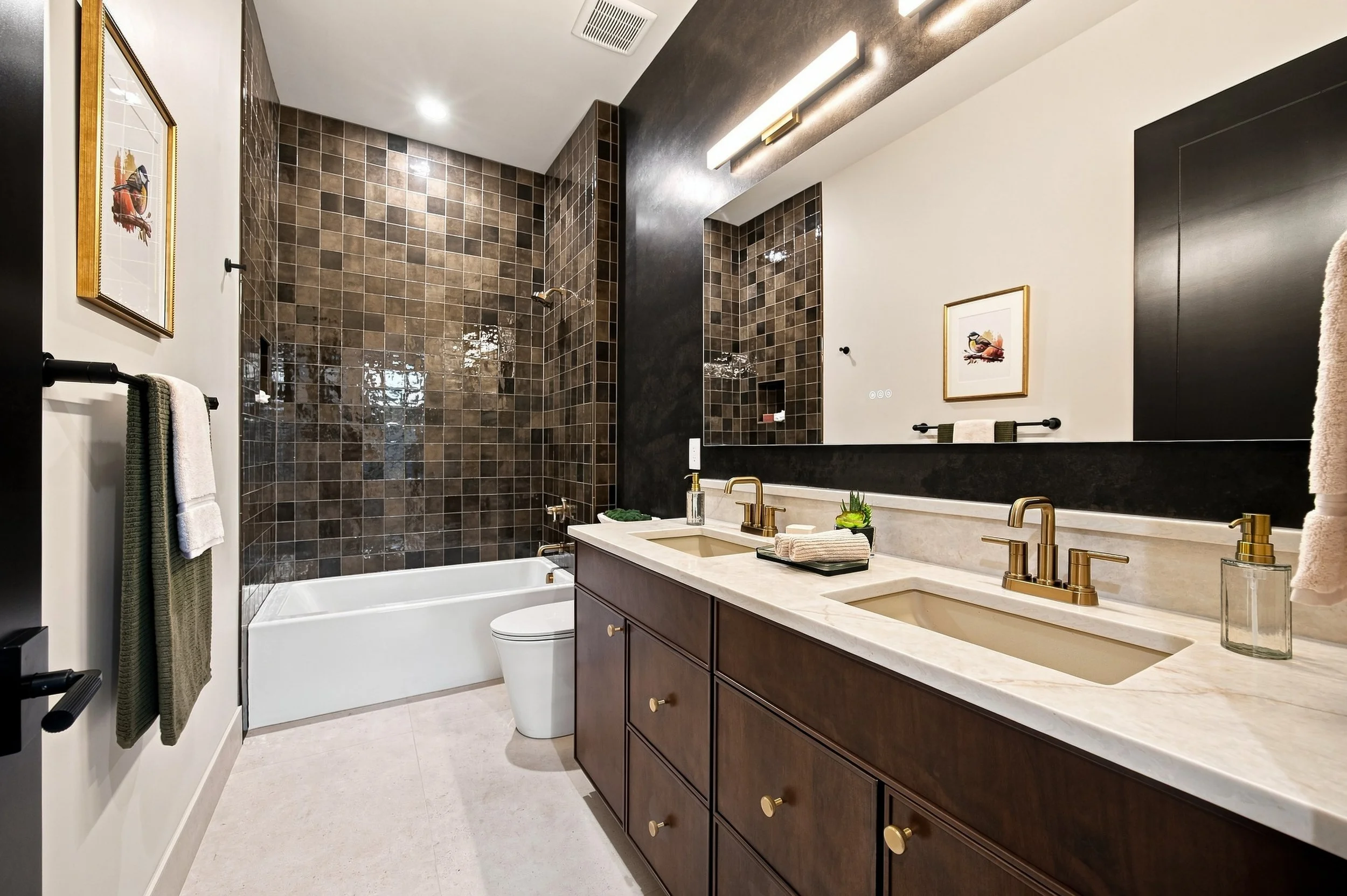 Hall bathroom with dark patterned tile, a bathtub, and wood vanity.
