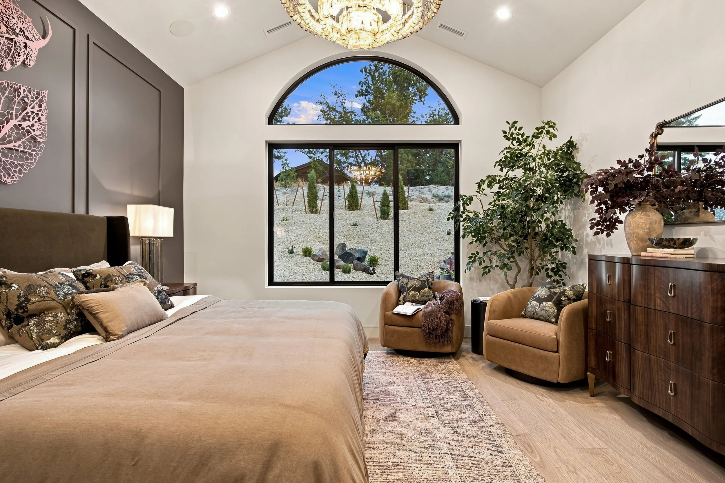 Primary bedroom with a tall arched window and layered neutral furnishings.