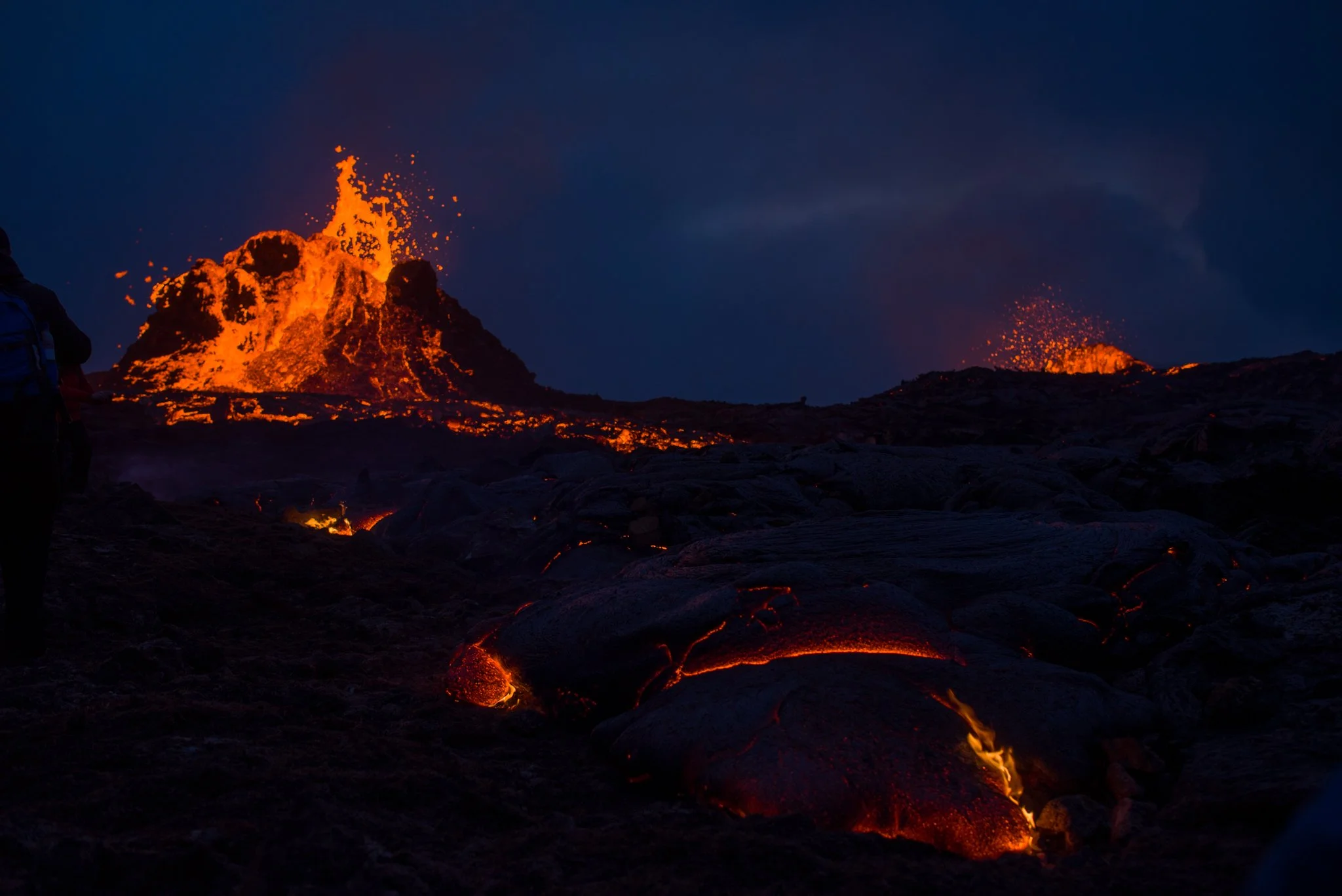 Eruption of lava from a volcano at night with glowing molten rock and ash falling.