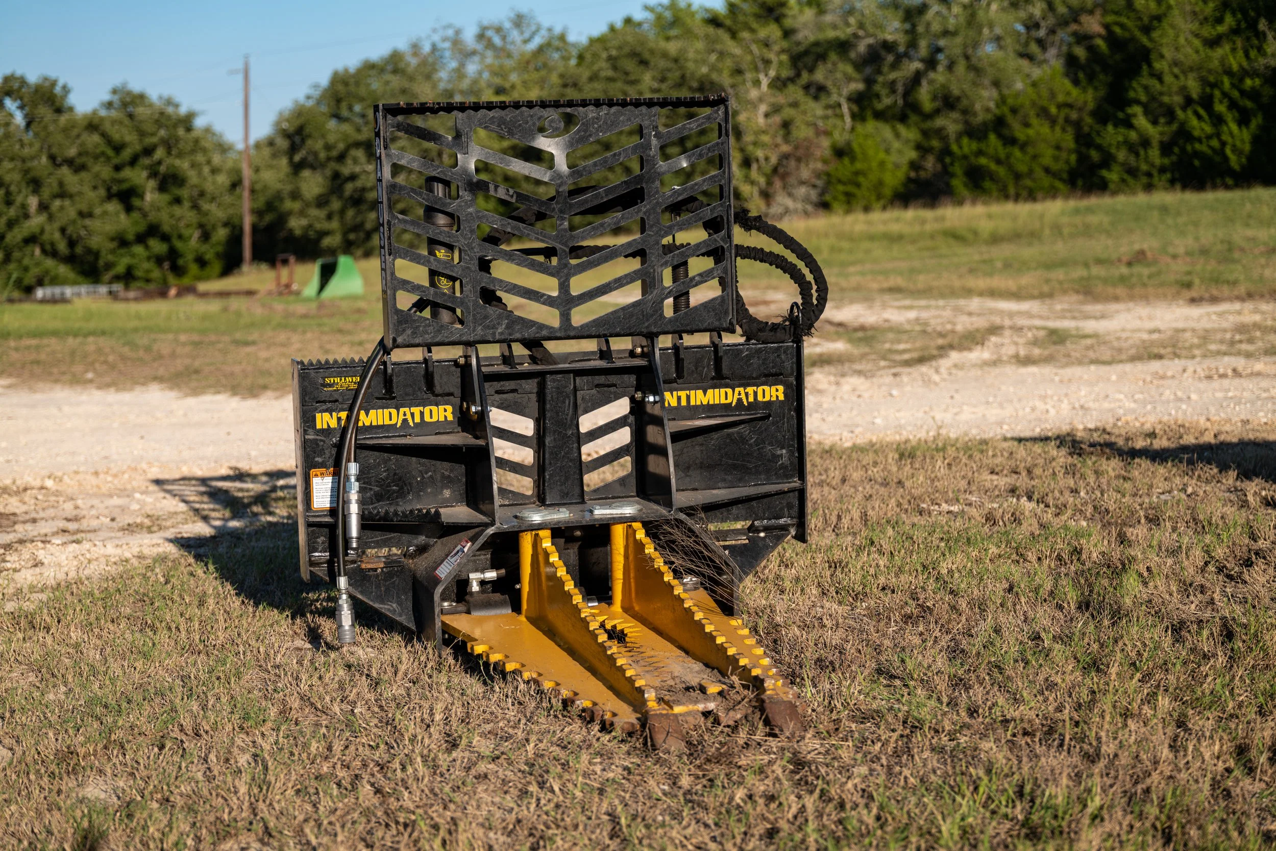 A piece of heavy-duty landscaping equipment known as the Intimidator tree and post puller attachment on a grassy field, used for removing trees and posts.
