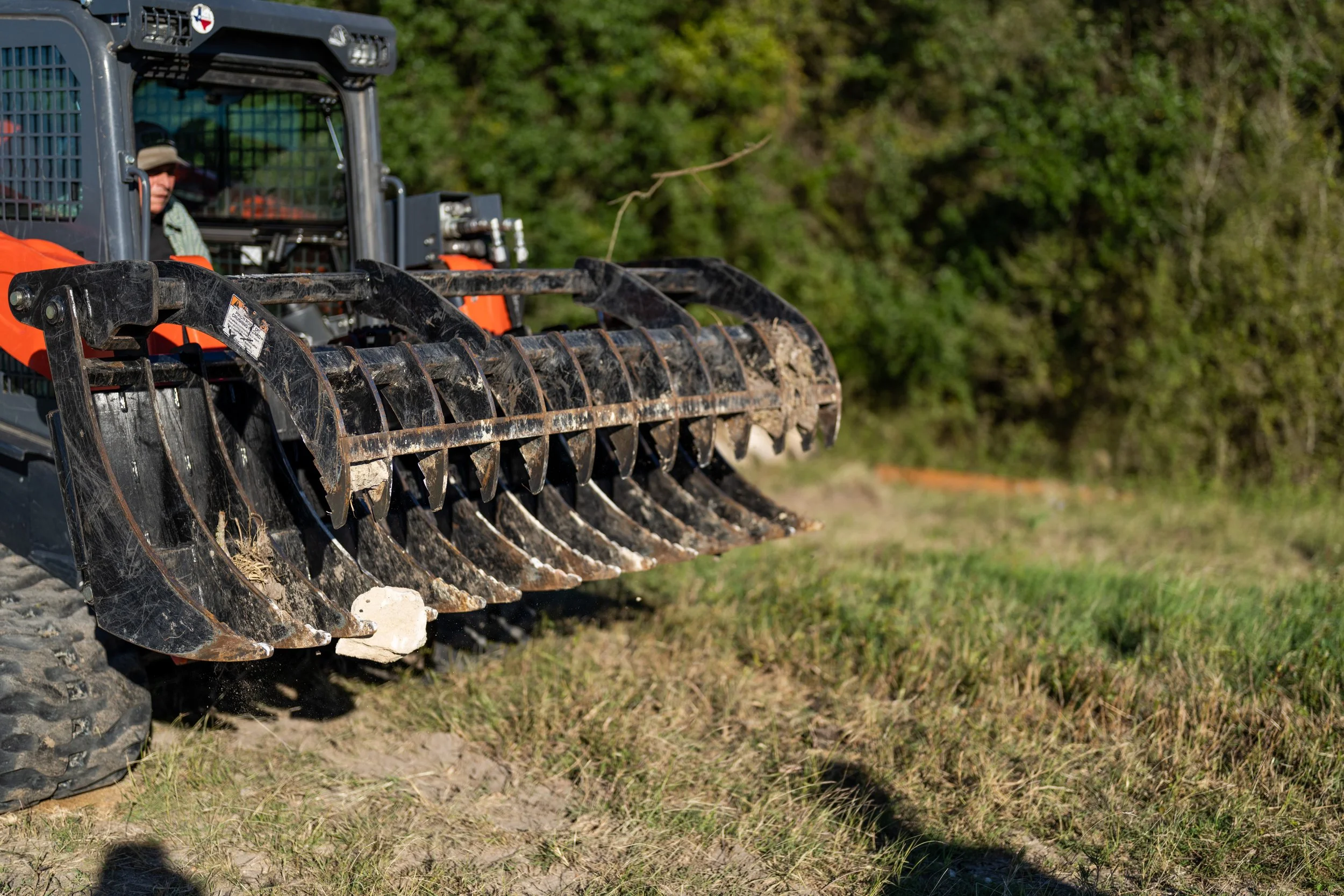 A construction vehicle with a grapple attachment in a field.