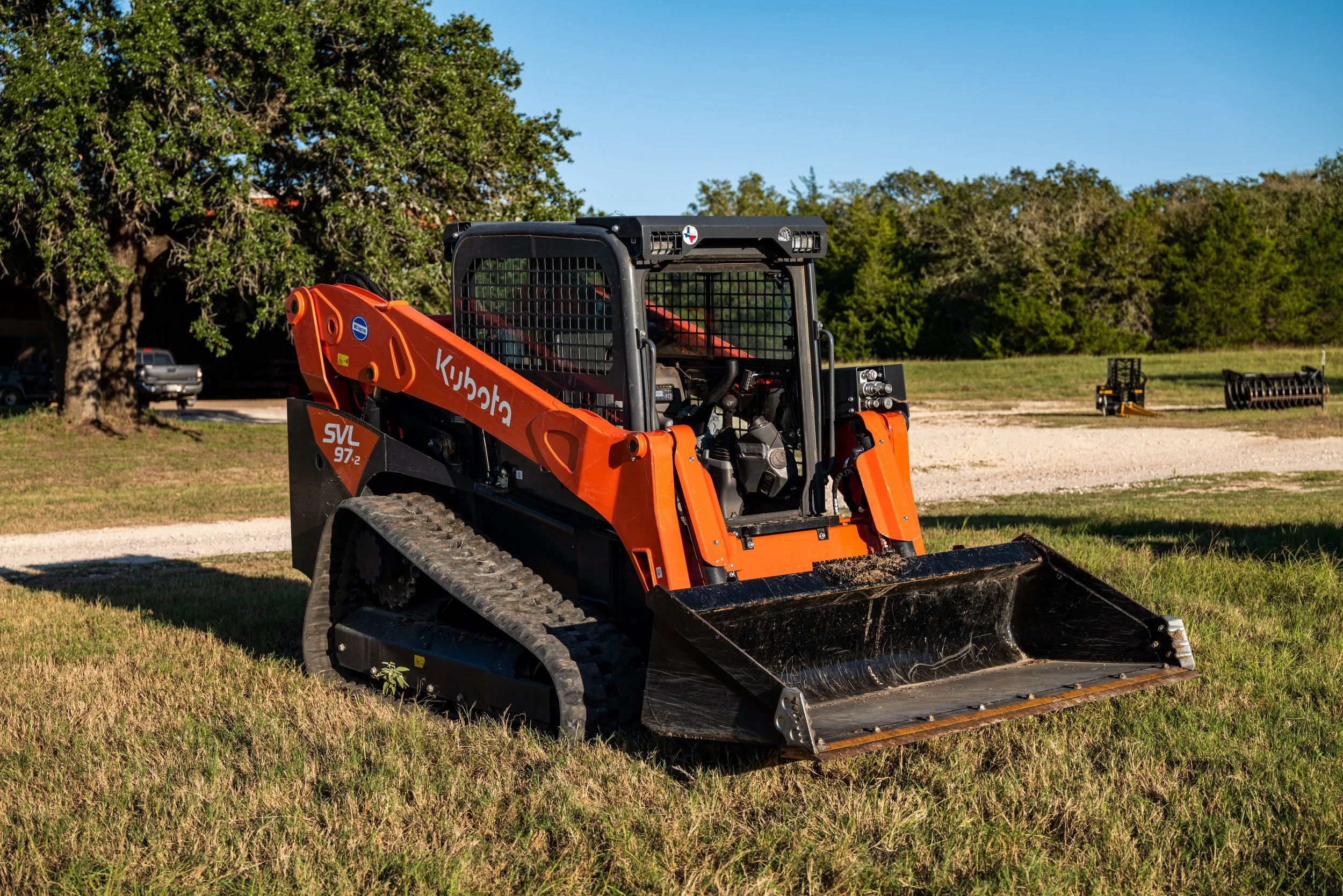 Orange Kubota SVL97-2 compact track loader on grassy field with trees in the background.