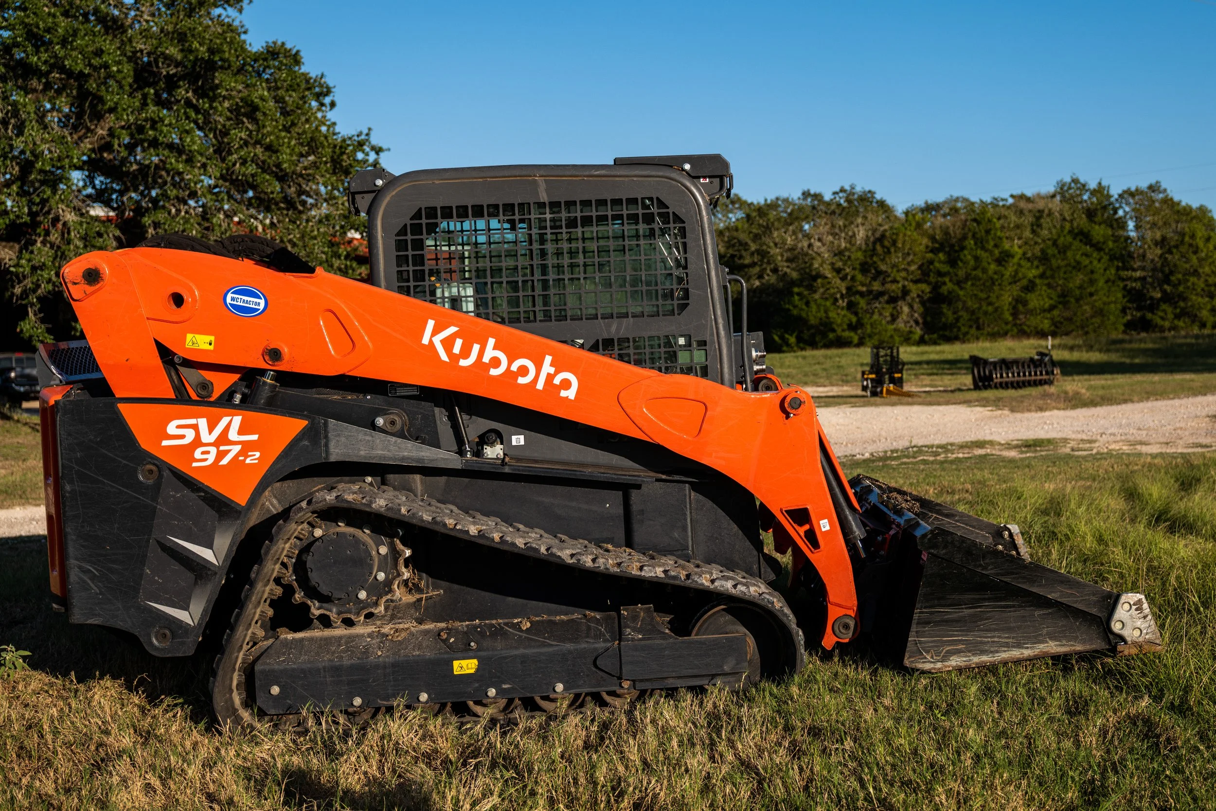 Kubota SVL97-2 compact track loader with orange and black design on grass.