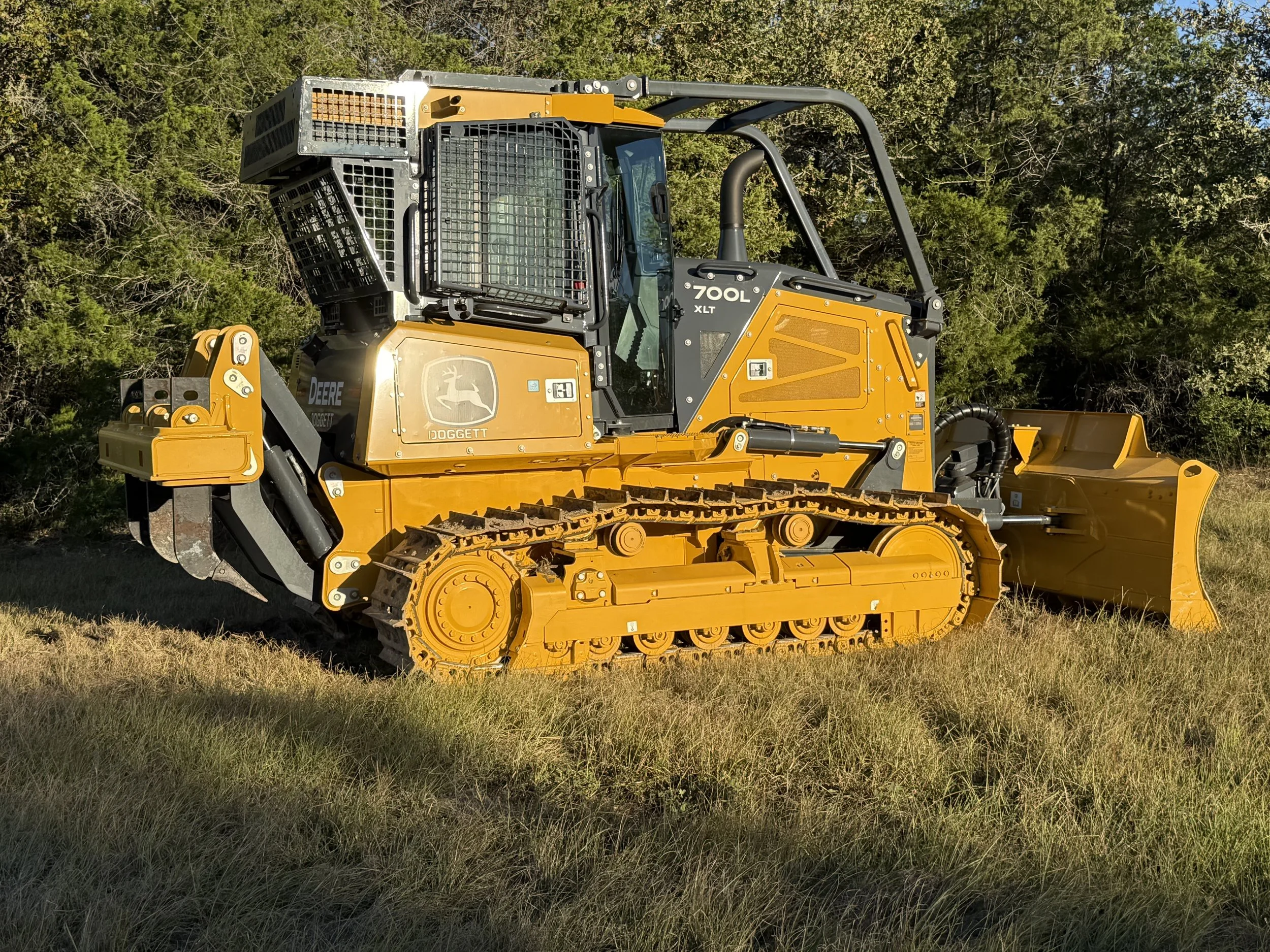 Yellow John Deere bulldozer with a blade attachment parked on grass near trees, provided by G-Quip Services LLC in the Brazos Valley, Texas.