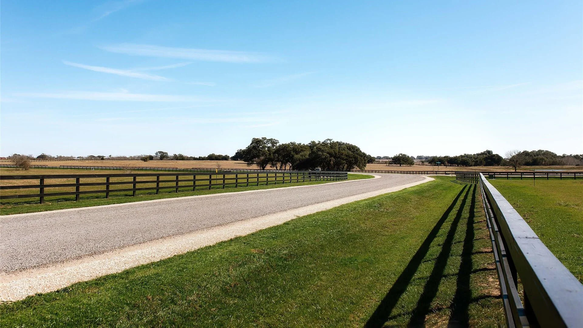 A rural road pathway curves through a grassy field, bordered by black wooden fences on either side, in Round Top, Texas with Country Communities, provided by G-Quip Services LLC in the Brazos Valley, Texas.