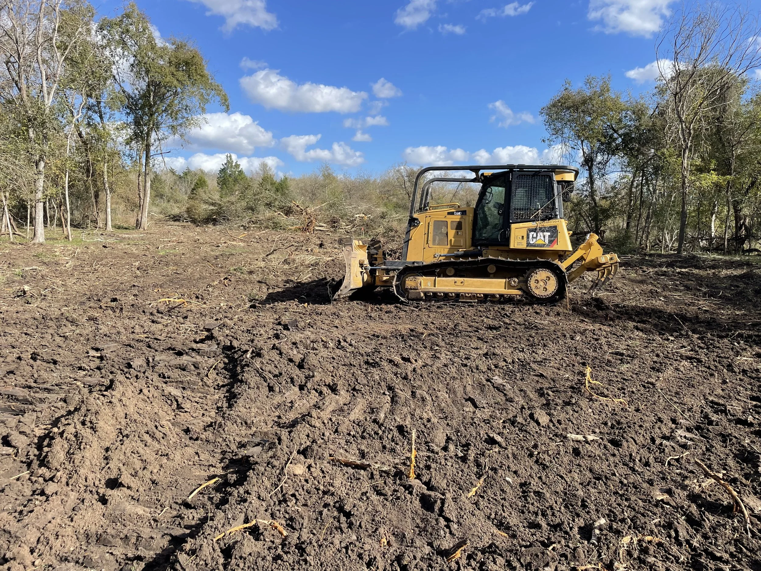 Yellow bulldozer working on a cleared land area with trees and a blue sky in the background, provided by G-Quip Services LLC in the Brazos Valley, Texas.