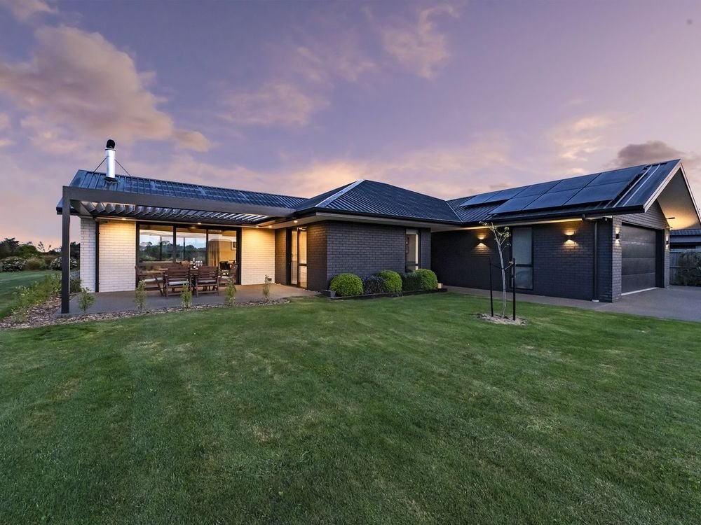 Contemporary single-storey home opening onto a garden and outdoor dining area at dusk