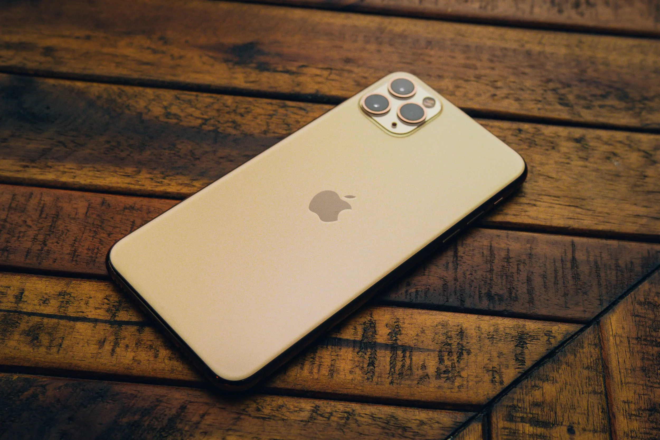 A white iPhone with three camera lenses on the back, lying on a wooden surface.