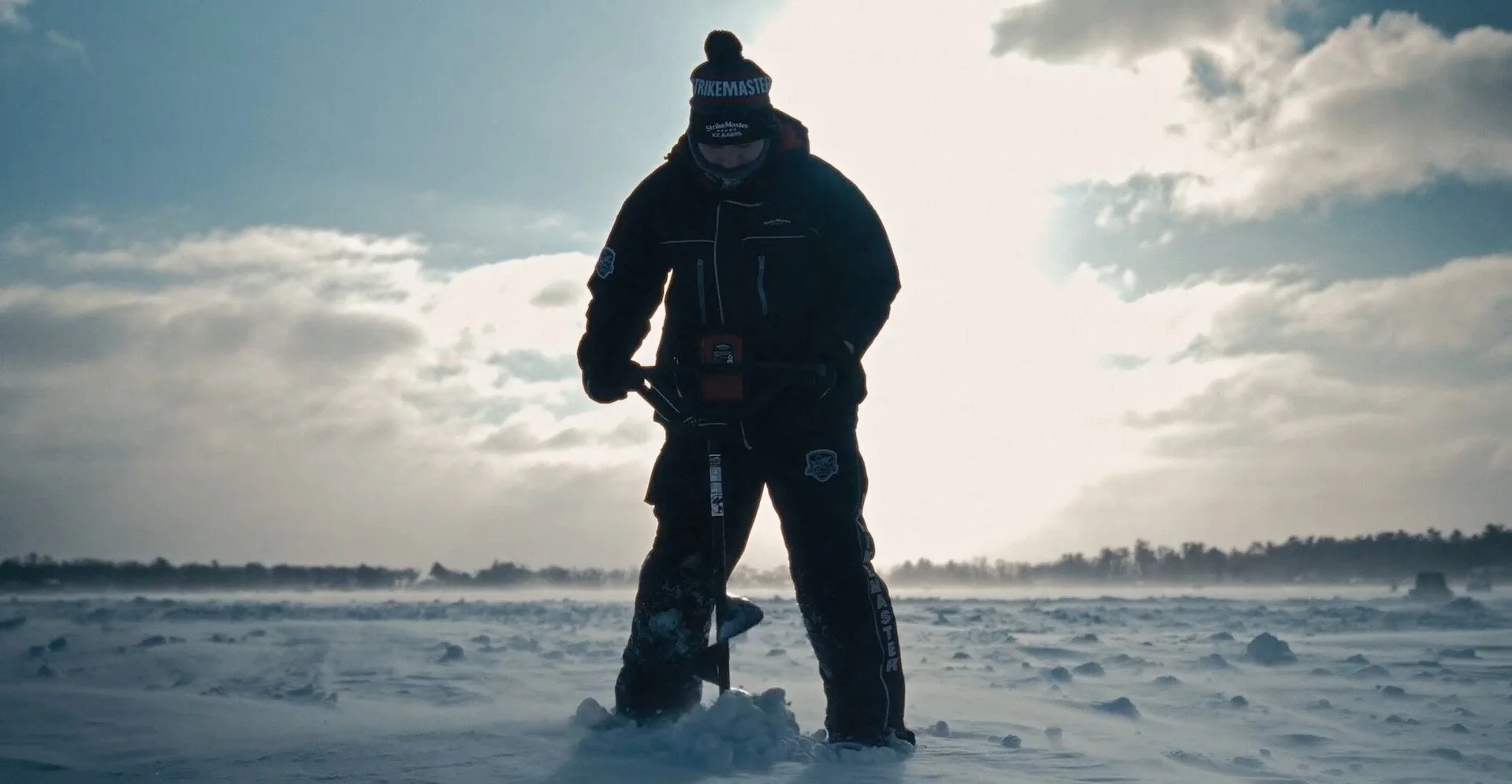 Silhouette of a person in winter gear standing on snowy ground with a cloudy sky behind them