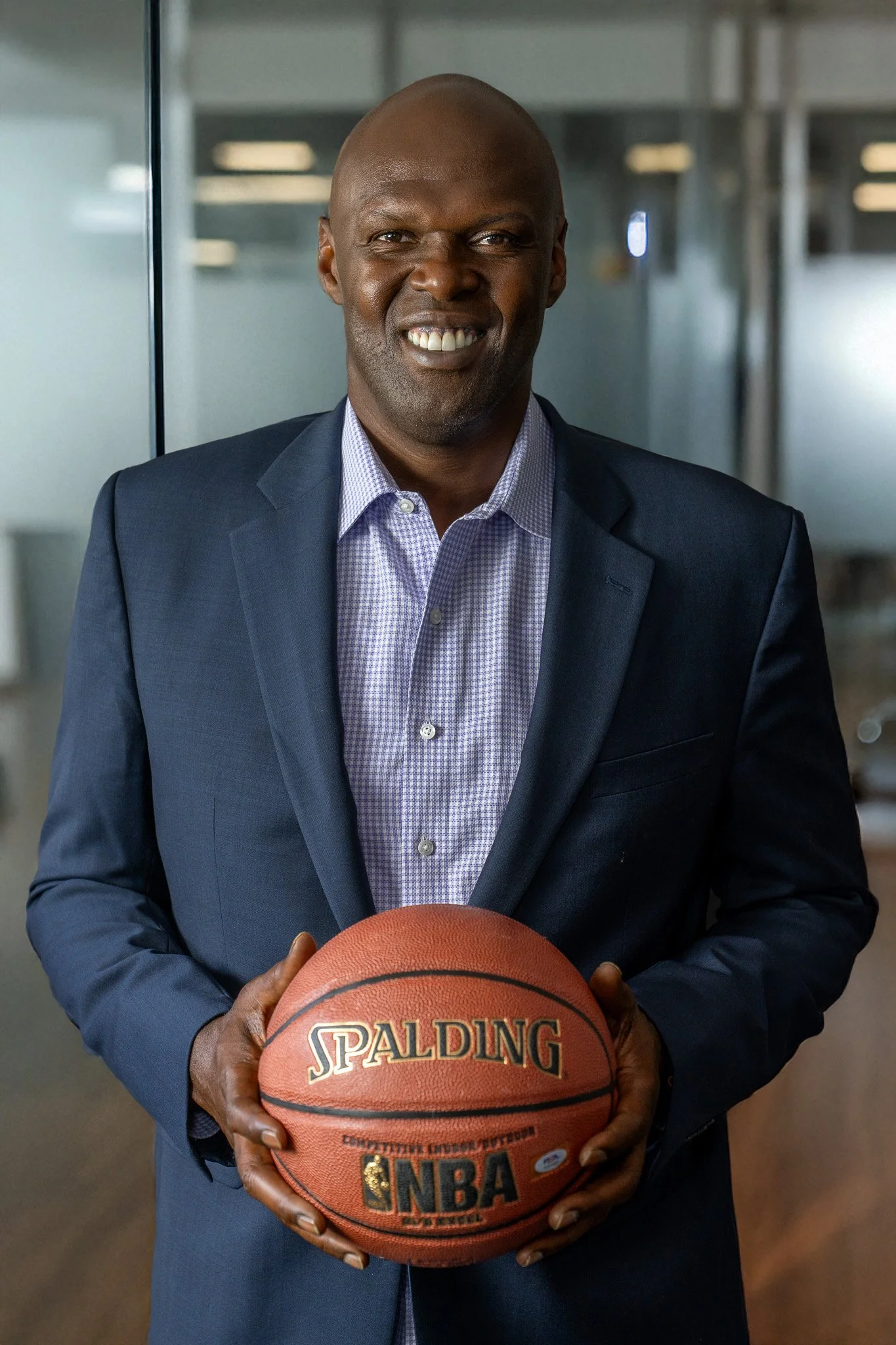 Adonal Foyle in a suit holding a Spalding NBA basketball in an indoor setting.