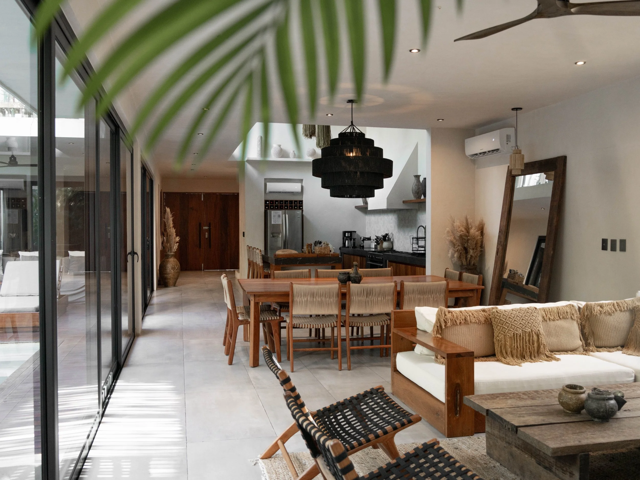 Open-concept living and dining room with wooden furniture, beige cushions, modern decor, large glass sliding doors, and a spacious layout.