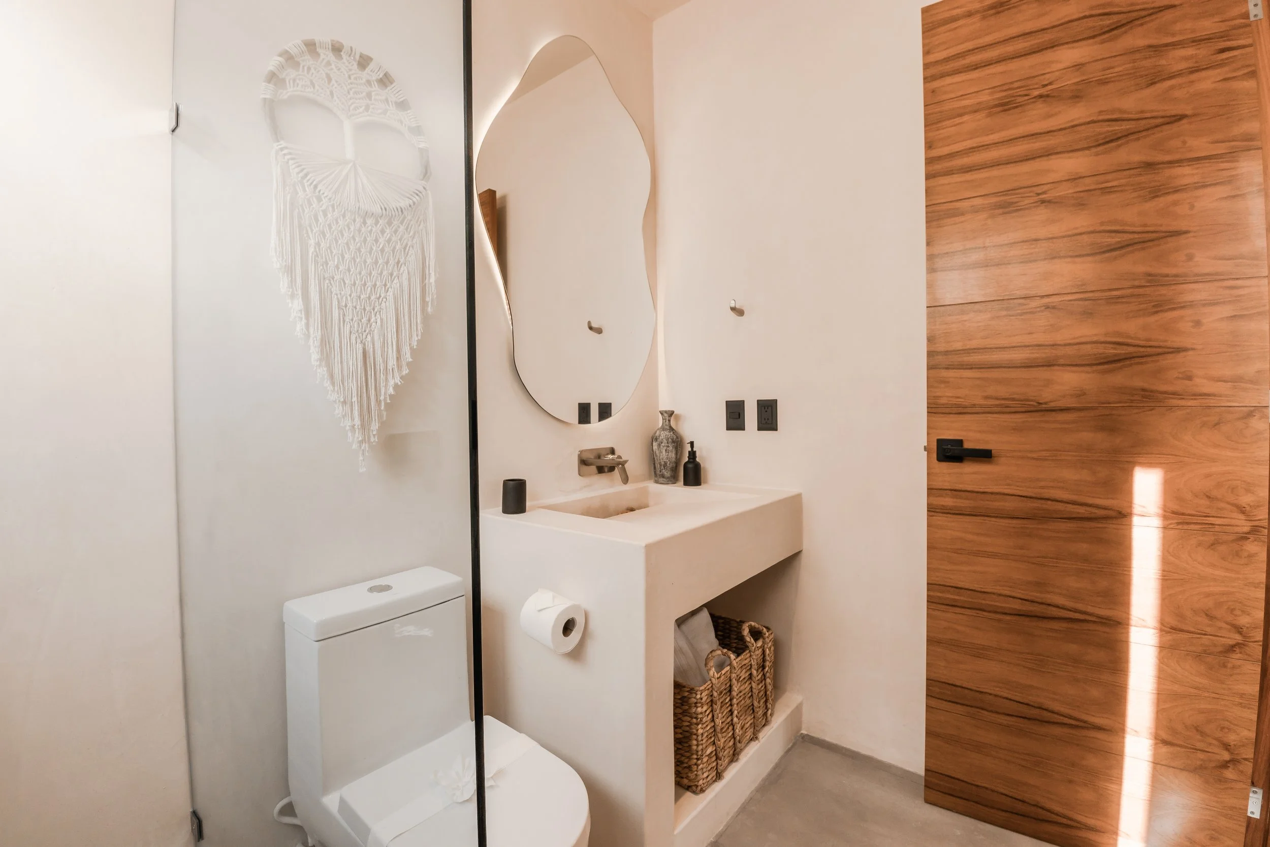Small bathroom with a toilet, a wall-mounted sink, an oval mirror, decorative vases, and a wooden door.