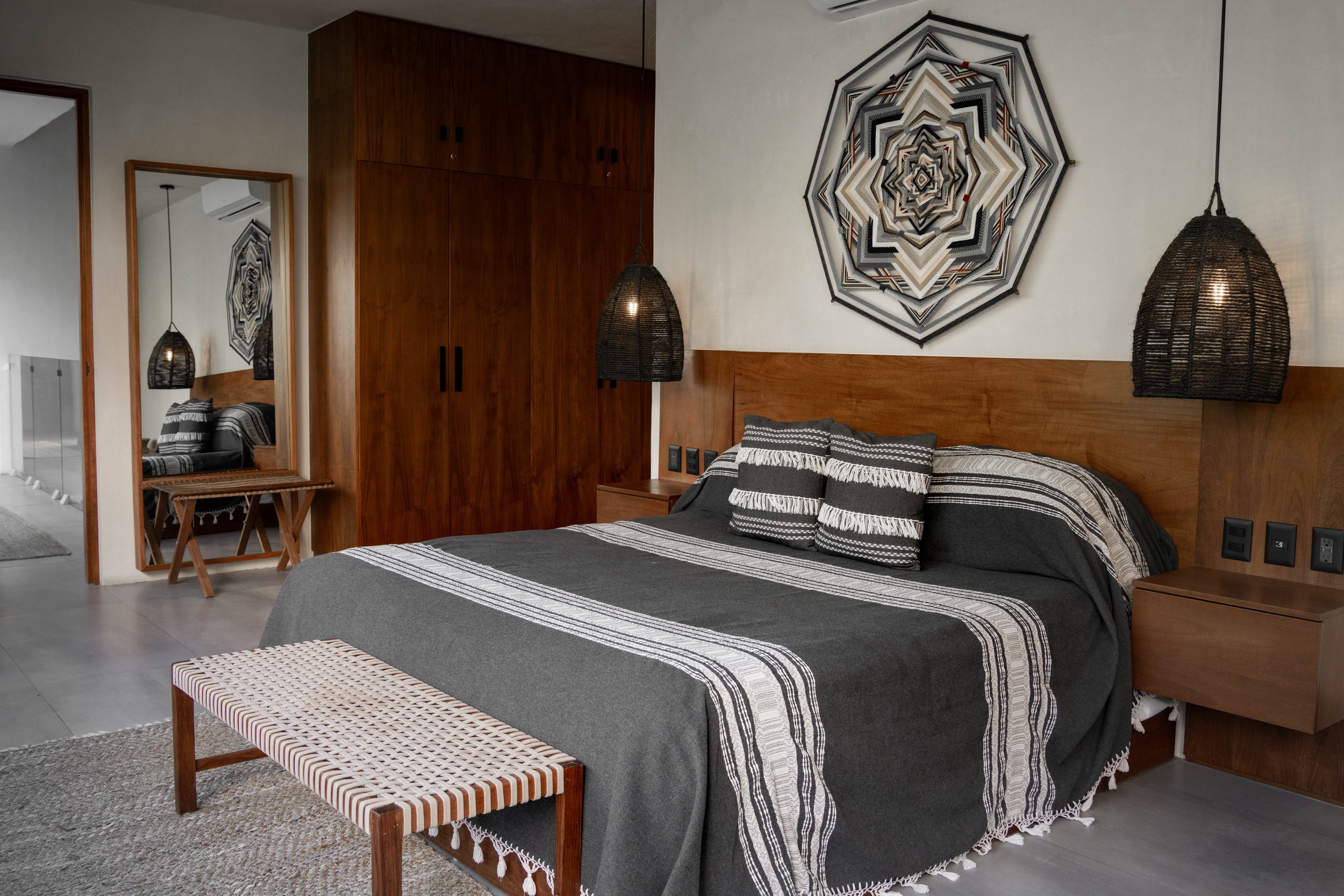 Modern bedroom with wooden accents, a patterned wall hanging, black and white bedding, pendant lights, and a full-length mirror.