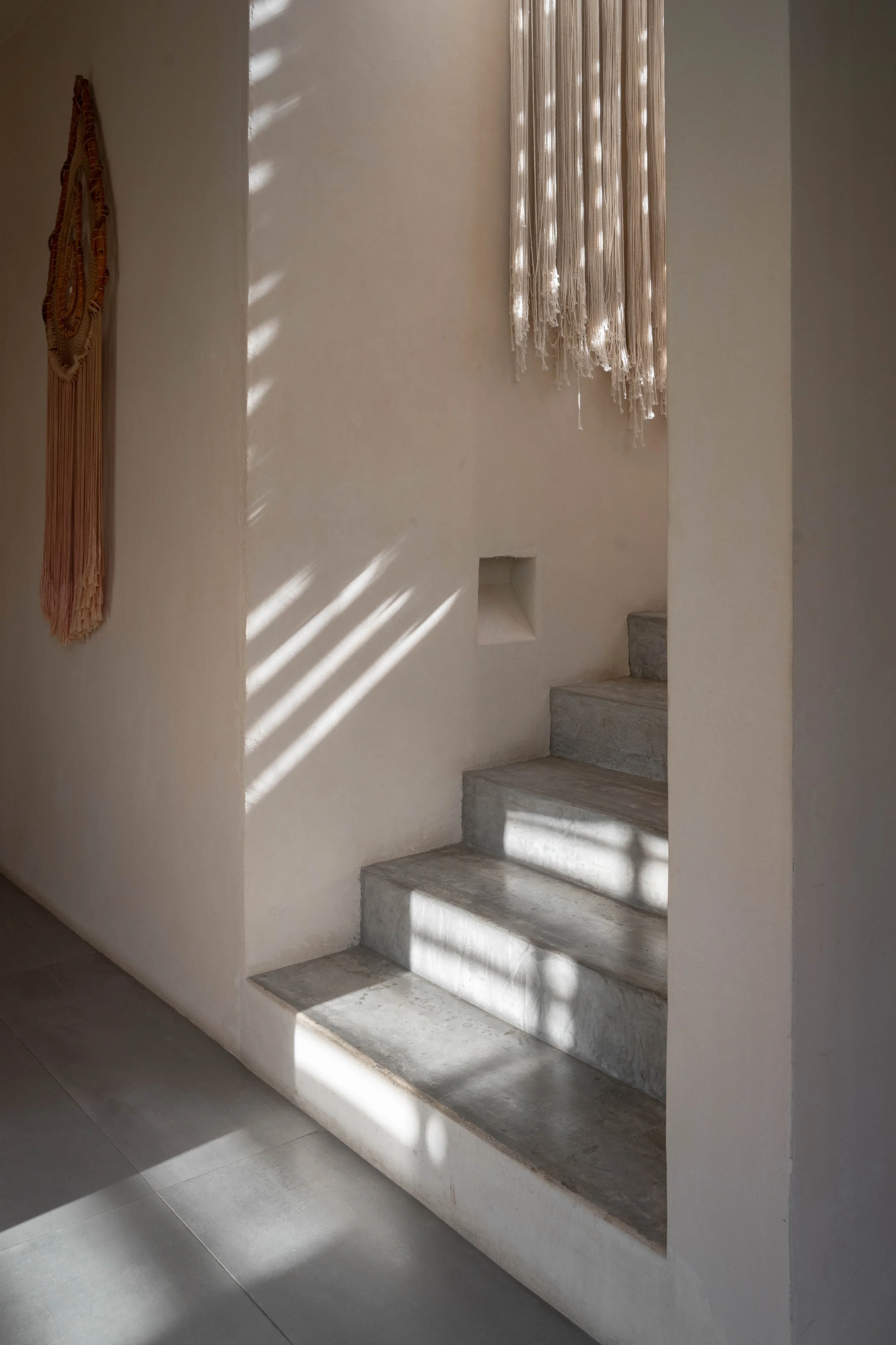 Concrete staircase with sunlight and shadow patterns on the steps, beige walls, and hanging fabric or curtain.